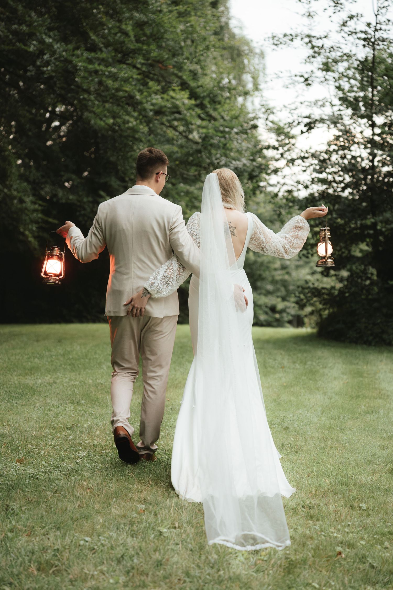 Couple strolling through garden holding lanterns at twilight.