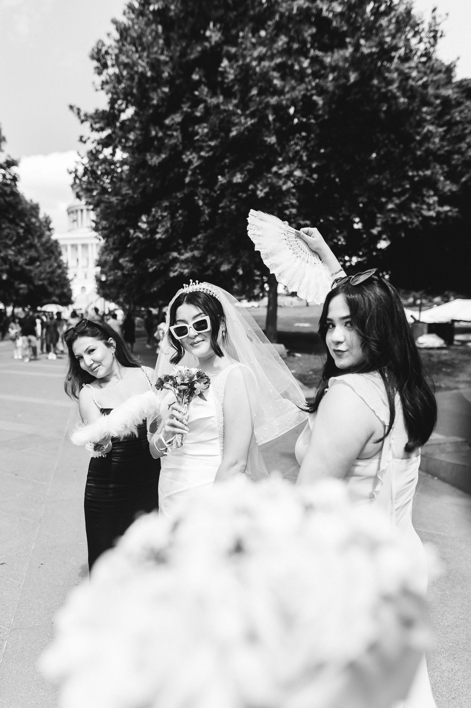 Black and white photo of a bride wearing sunglasses and veil posing with two bridesmaids outdoors.
