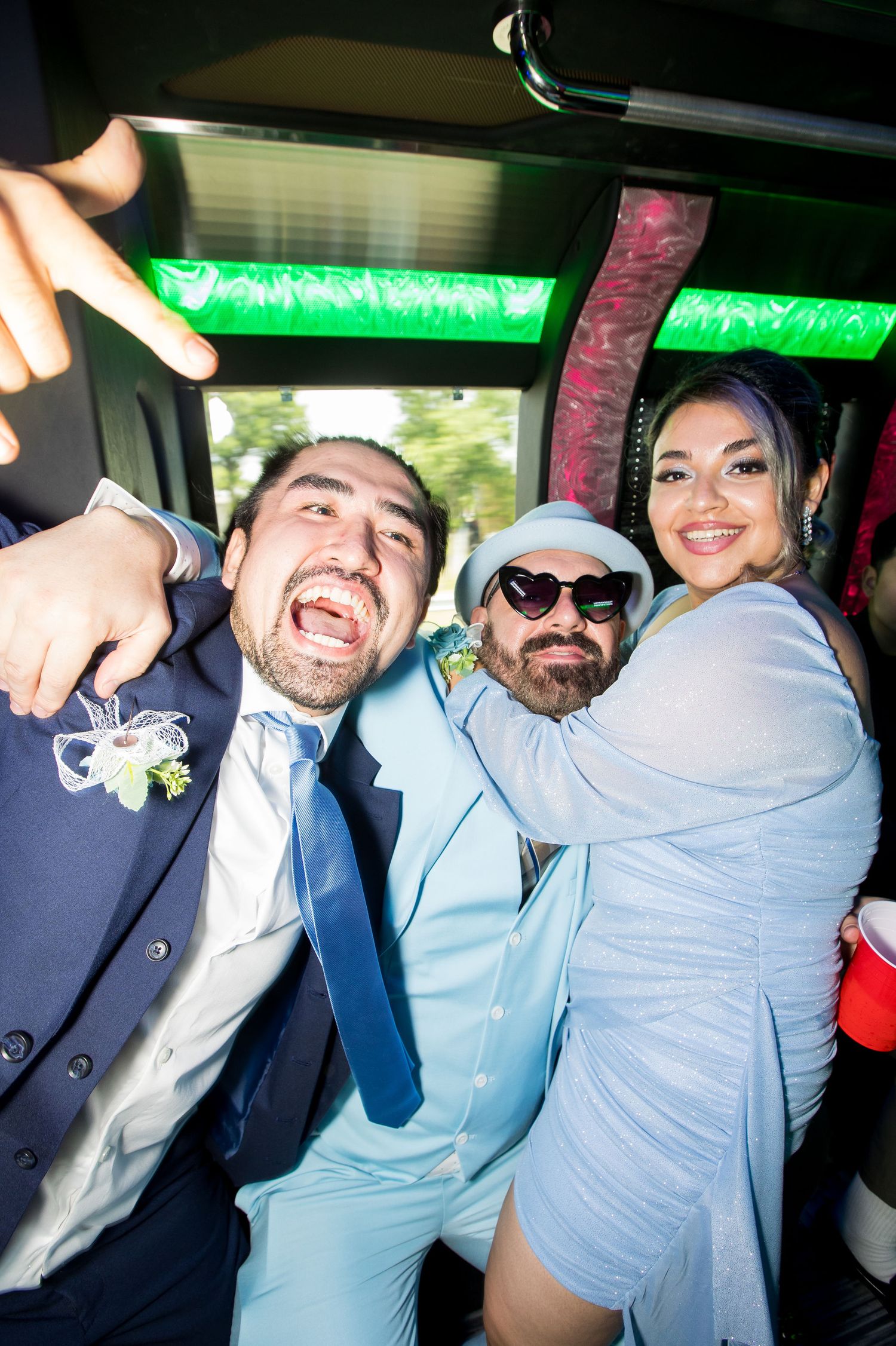 Three people celebrating on a party bus, two men in blue suits and a woman smiling, at a festive wedding event.