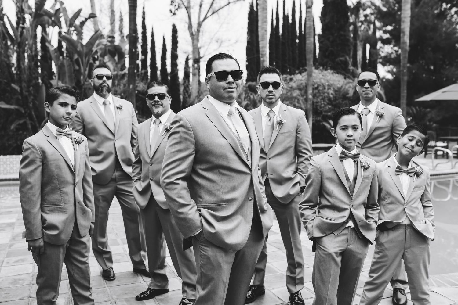 Groomsmen in matching gray suits and sunglasses pose confidently outdoors at a wedding.
