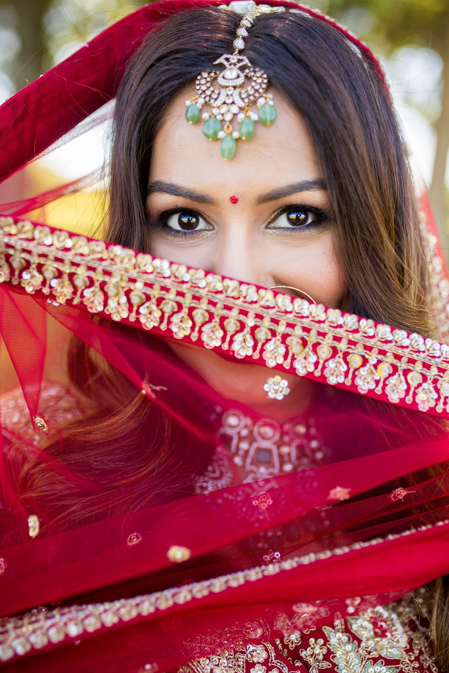 Indian bride in red lehenga and dupatta with maang tikka jewelry, showcasing traditional bridal look.