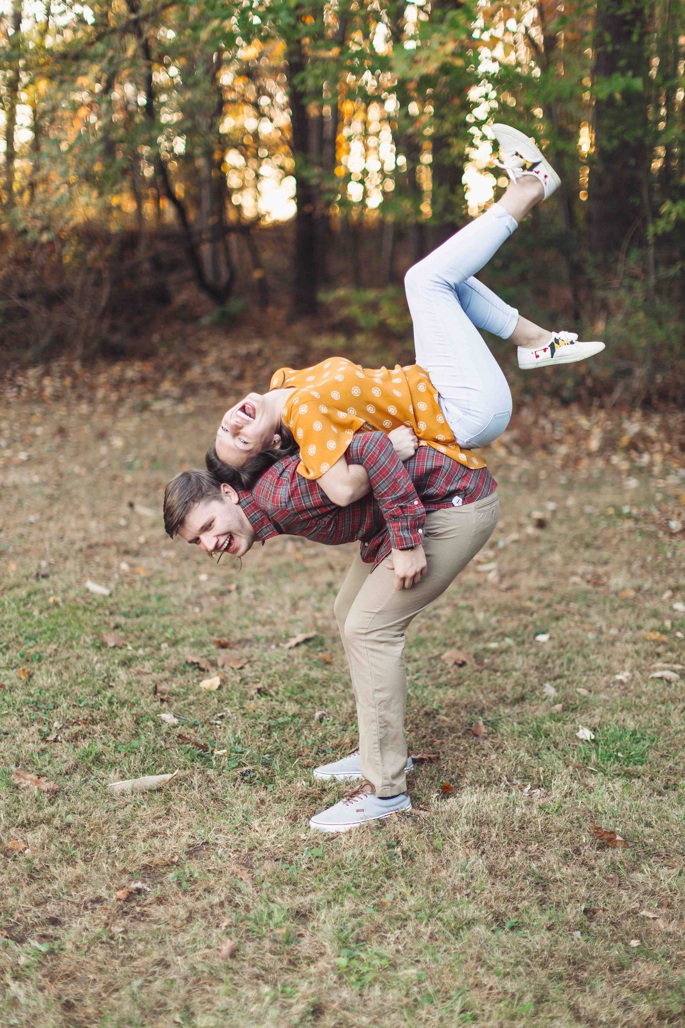 A man playfully carries a laughing woman on his back in an autumn forest setting.