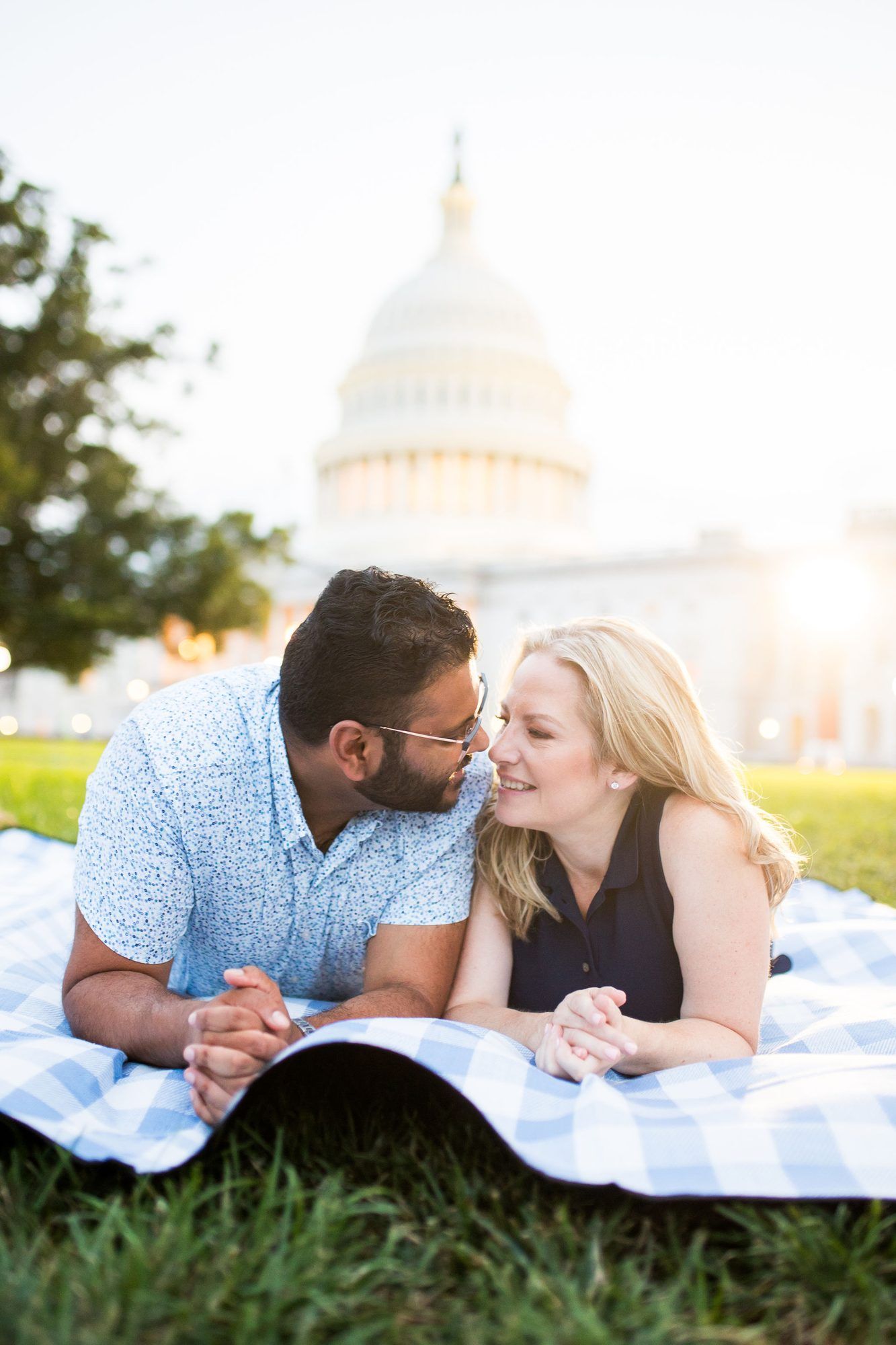 Couple lying on a blanket sharing a romantic moment with the U.S. Capitol building in the background.