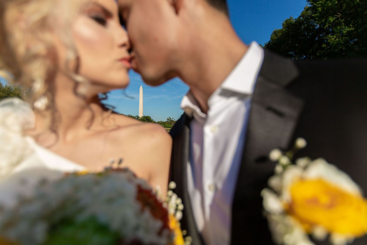 Bride and groom kissing with Washington Monument in background at outdoor wedding ceremony.