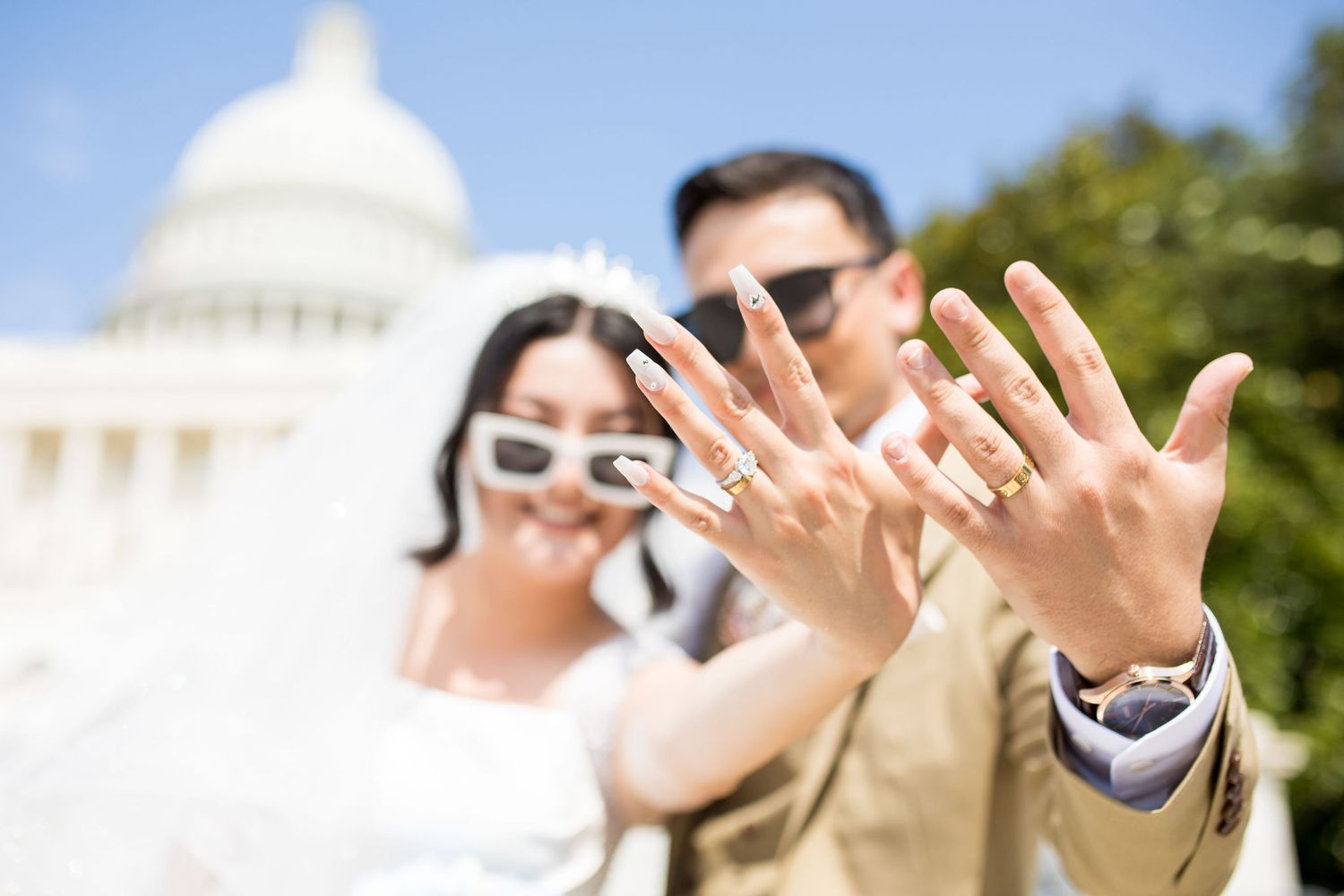 Newlyweds showing off wedding rings in front of US Capitol building on sunny day.
