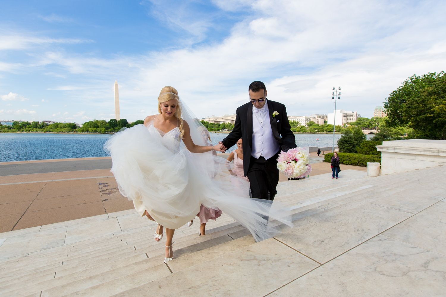 Bride and groom walk up marble steps near the Washington Monument and Tidal Basin on their wedding day.