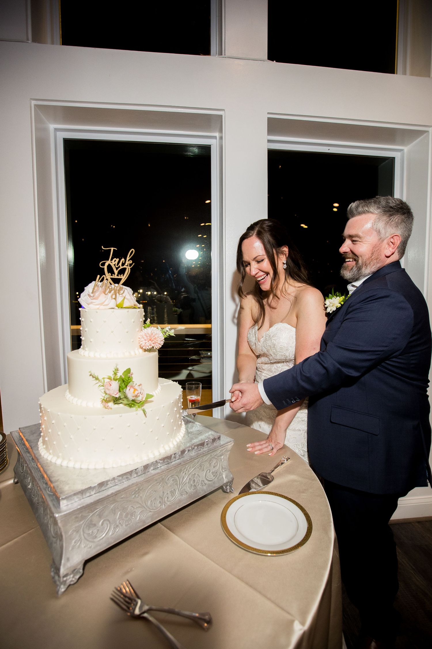 Bride and groom cutting their white three-tier wedding cake decorated with pink flowers at their reception.