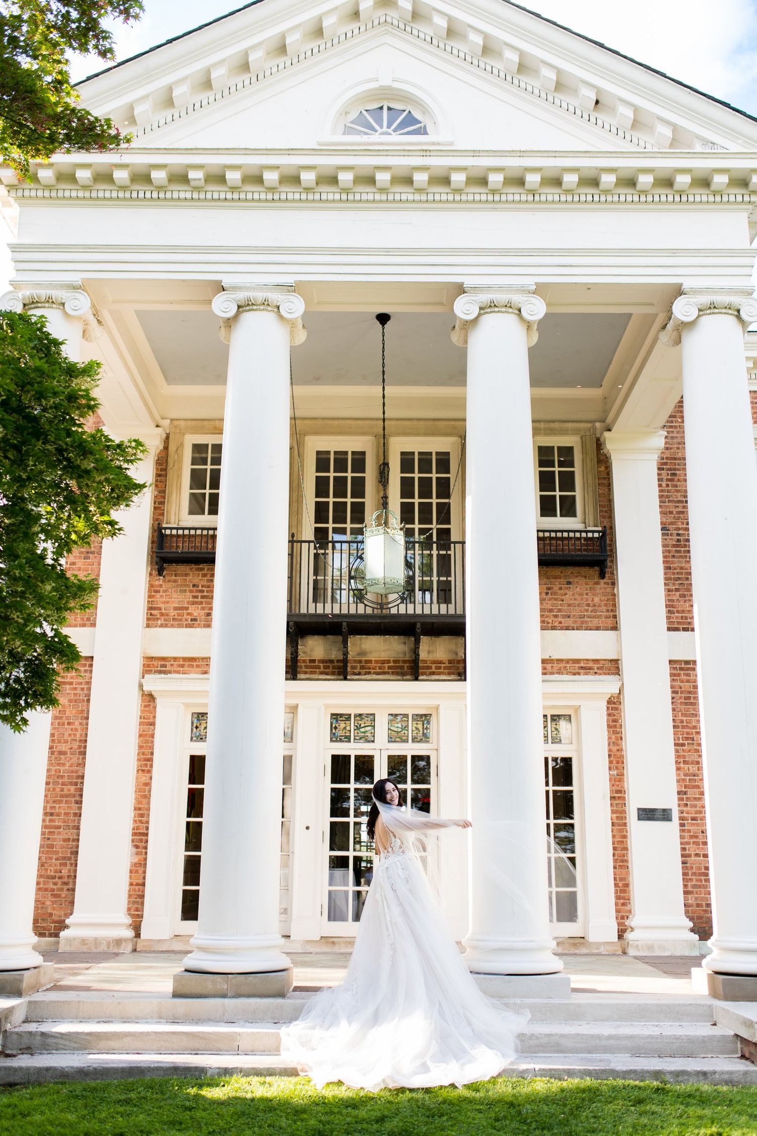 Bride and groom pose before a grand brick building with white columns and elegant architecture on their wedding day.