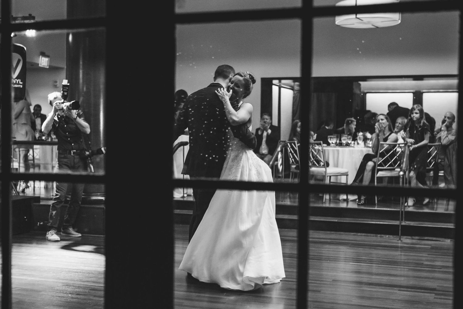 Black and white photo of bride and groom sharing first dance at wedding reception venue.