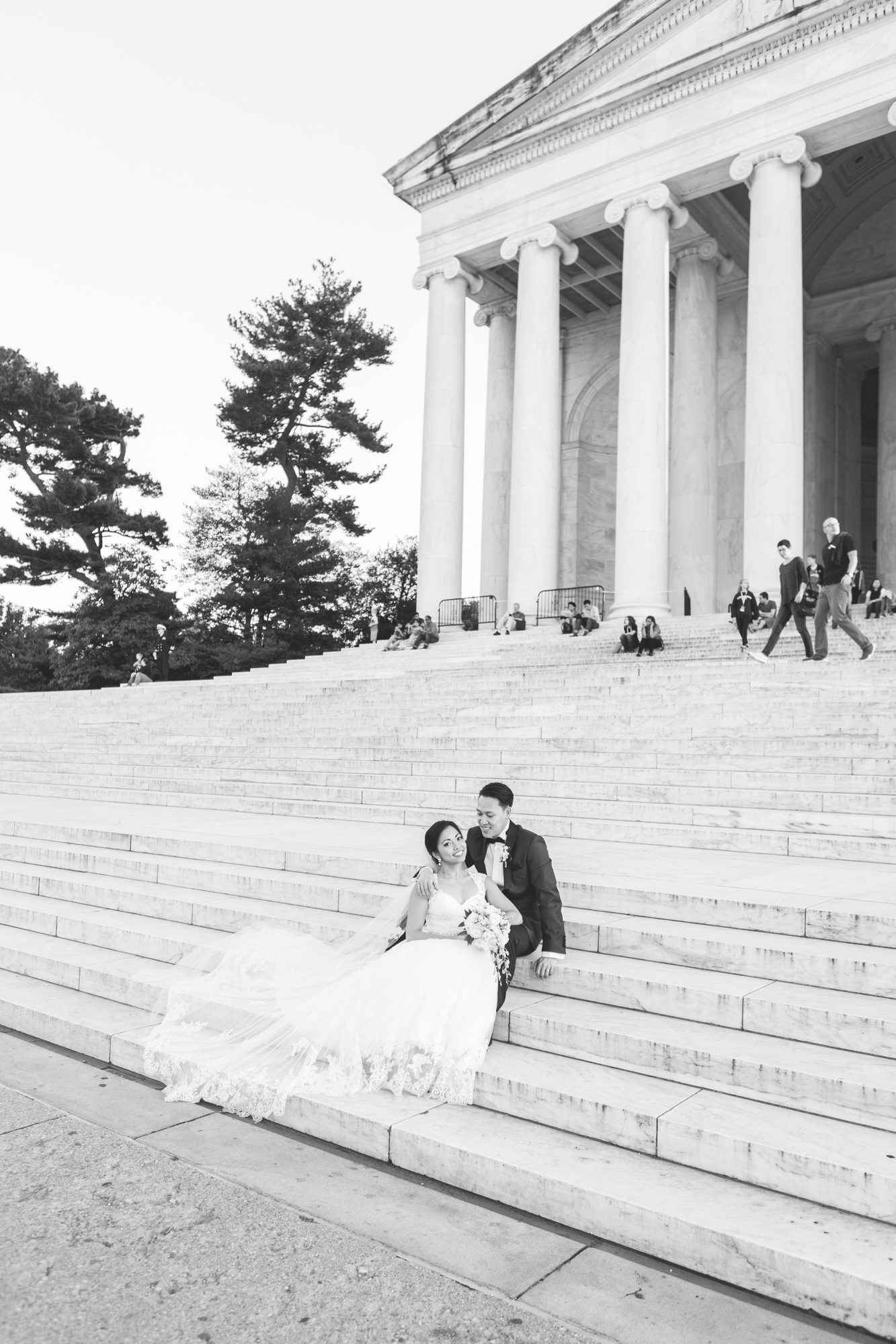 Black and white photo of a bride and groom sitting on the steps of the Jefferson Memorial on their wedding day.