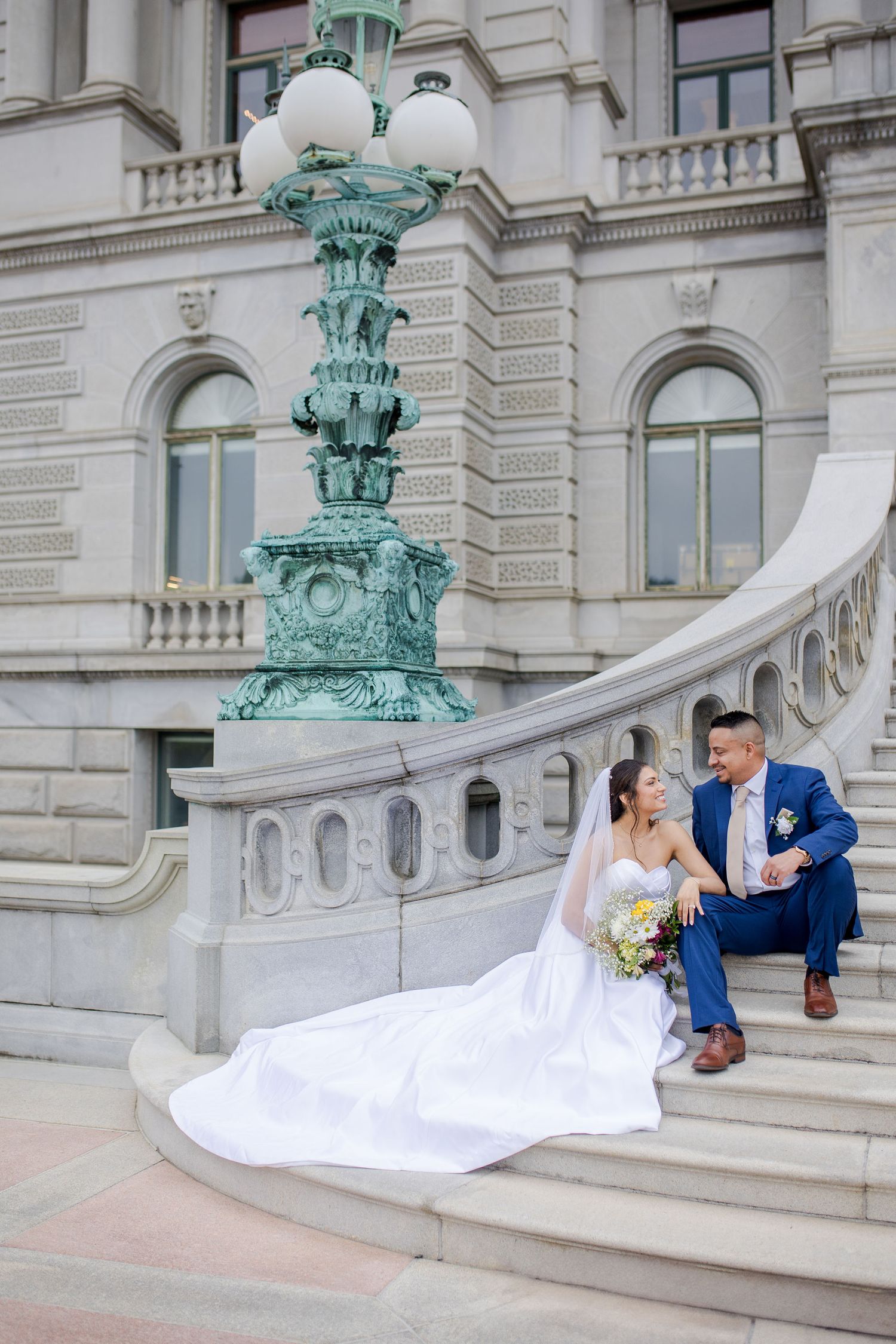 Bride and groom sitting on the elegant stone steps of the Library of Congress historic building with ornate green lamp post in Washington.