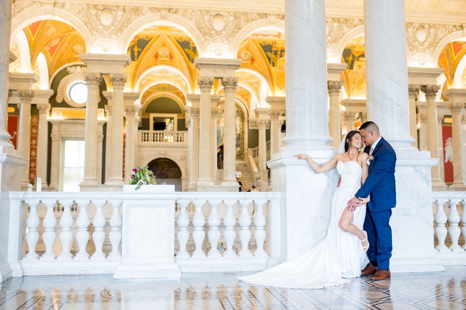 Couple sharing romantic embrace in ornate Library of Congress Great Hall with marble columns and gilded architecture.