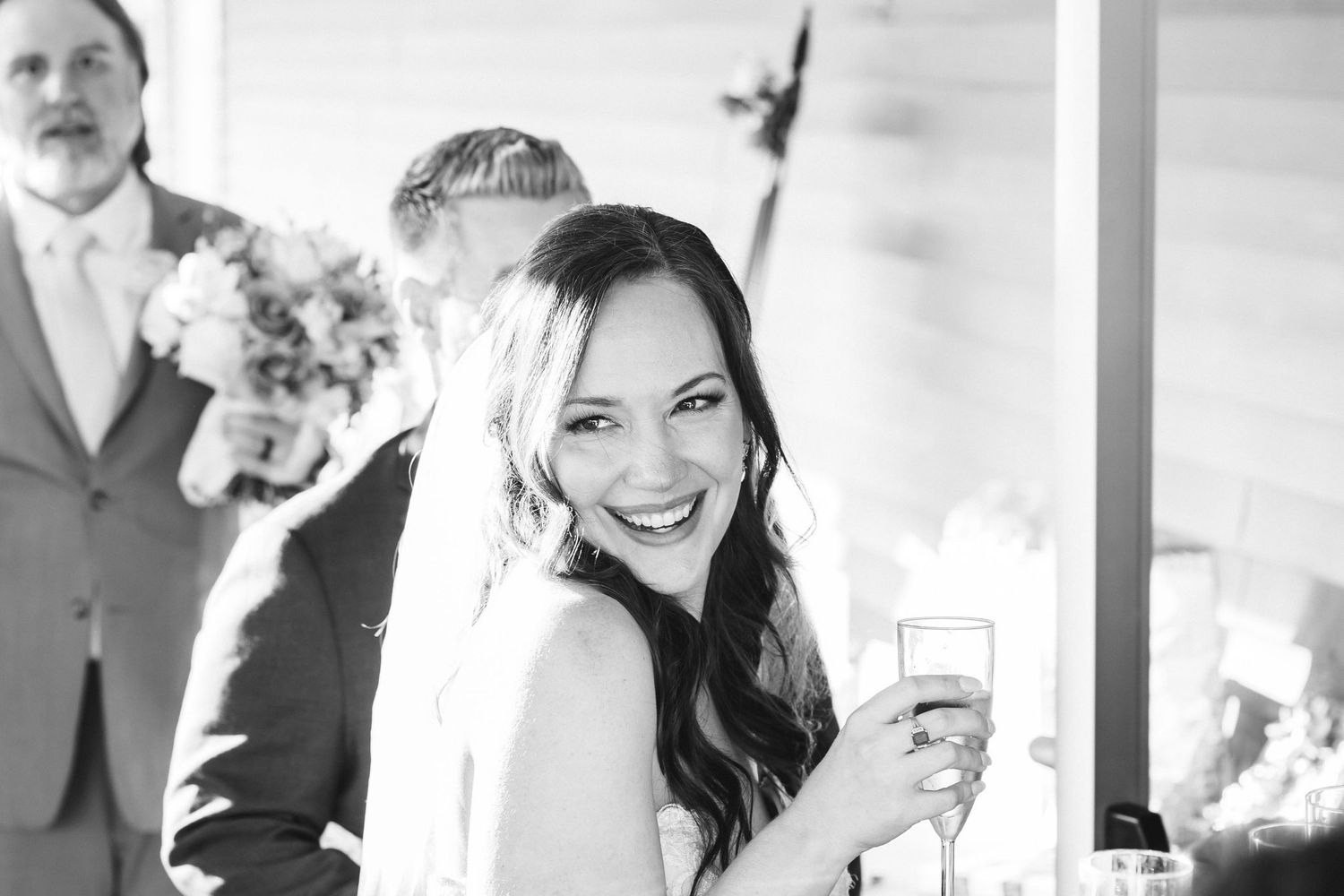 Smiling bride holding champagne glass at wedding reception in black and white photo.