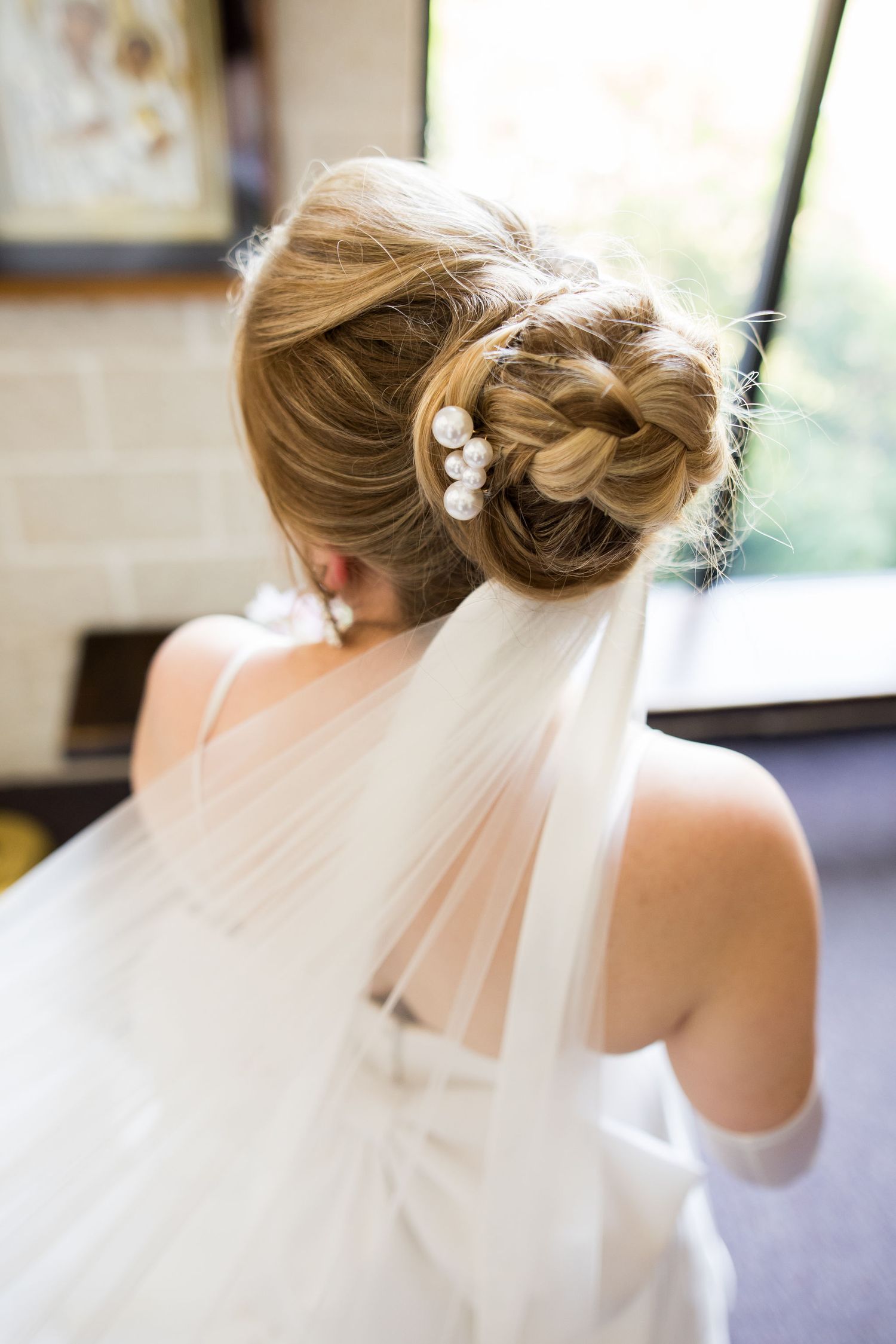 Elegant bridal updo with pearl hair pins and flowing white veil, viewed from behind.