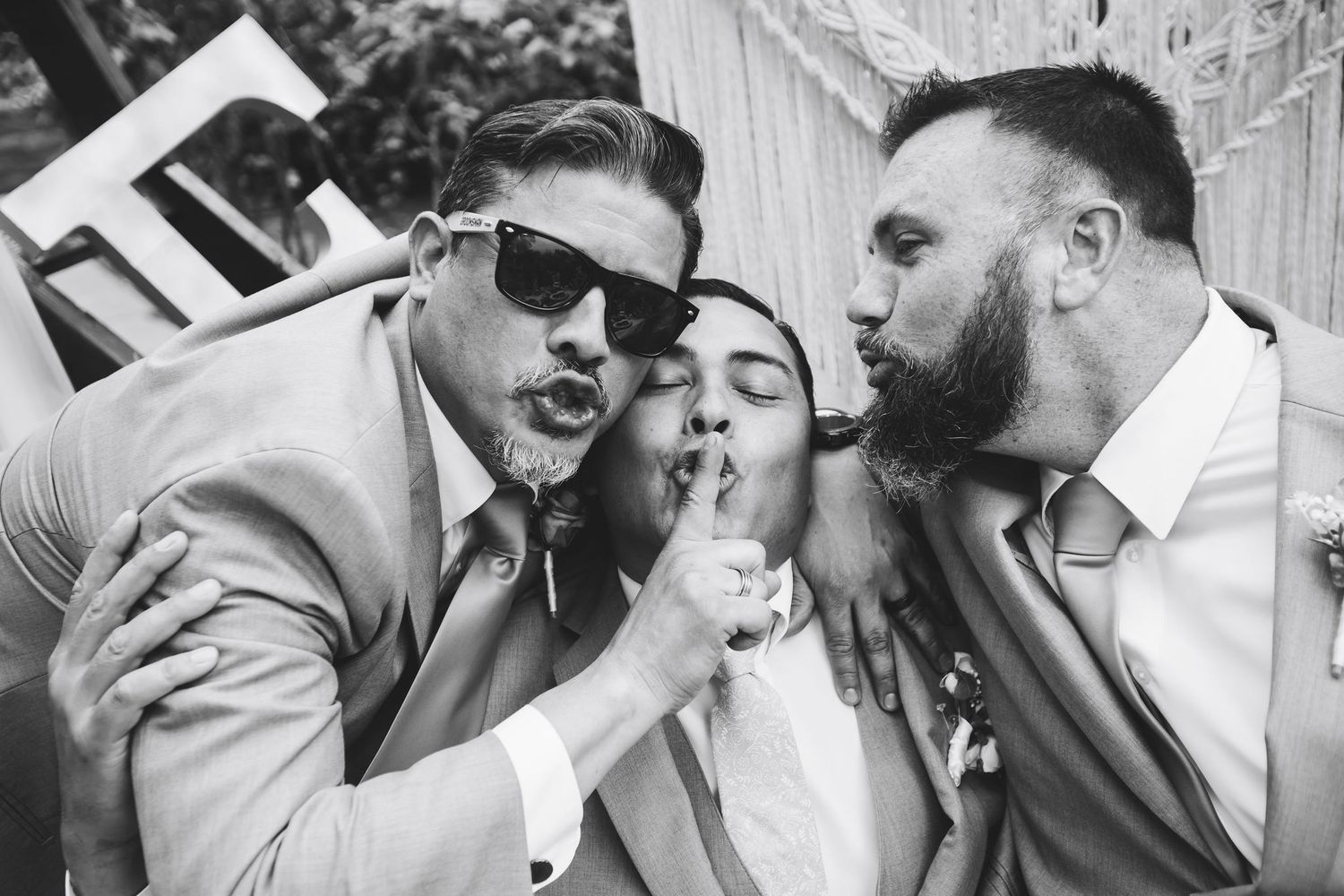 Three wedding guests playfully posing at photo booth in black and white image.