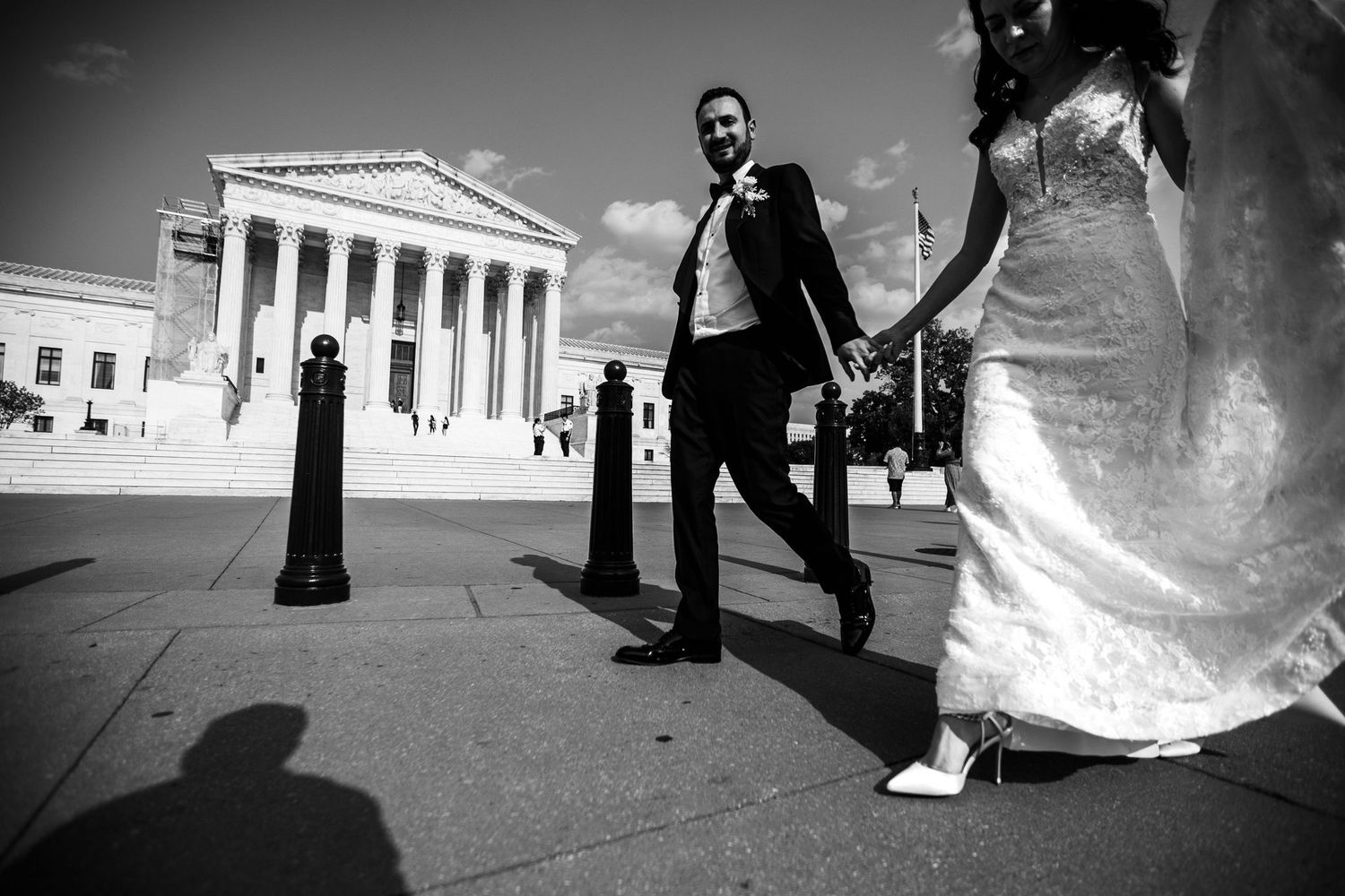 Black and white photo of a couple in wedding attire holding hands outside the US Supreme Court building.