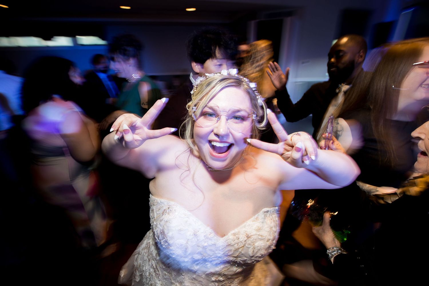 Bride in white gown making peace signs while dancing joyfully at a lively wedding reception party.