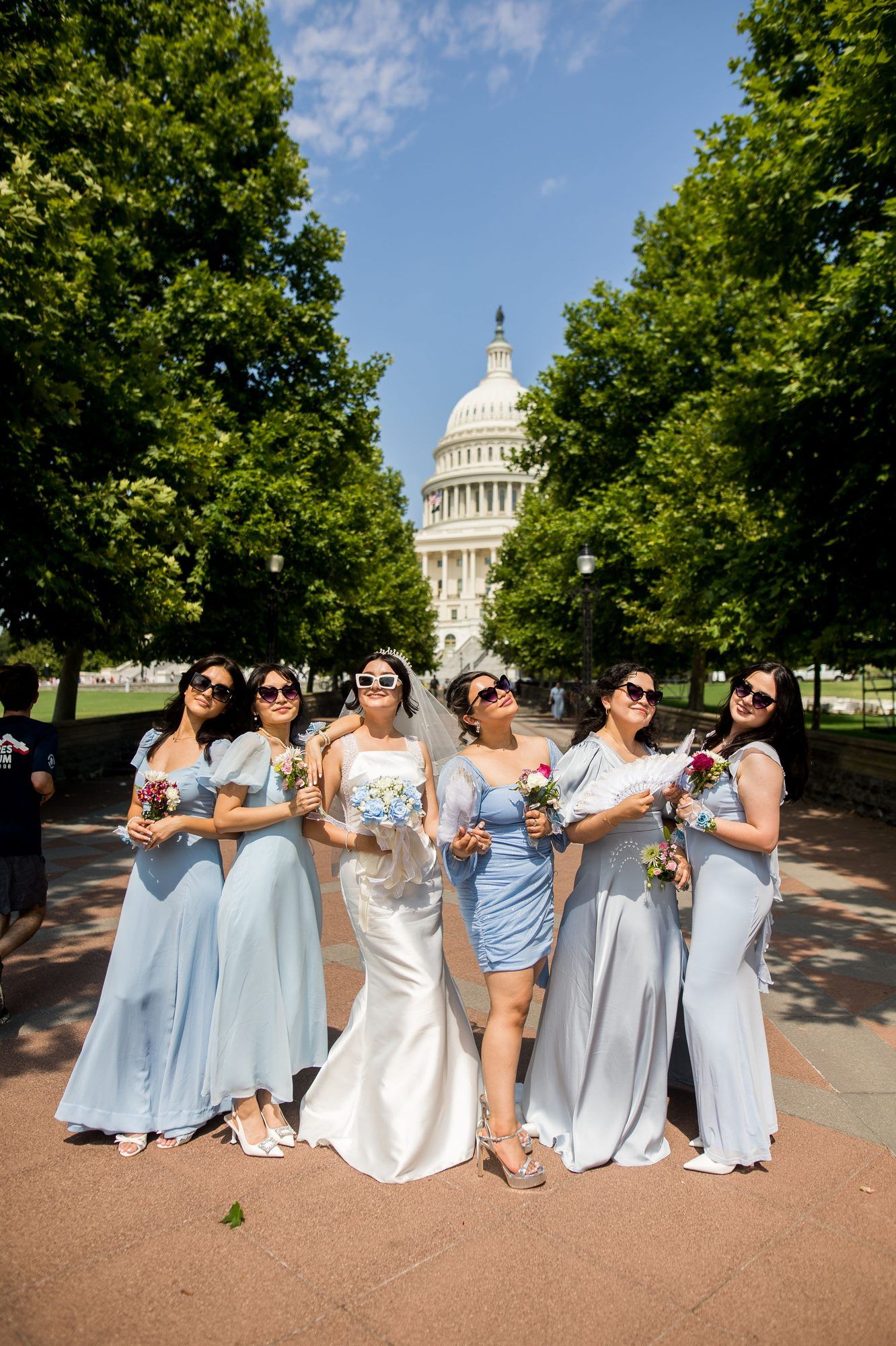 Bride and bridesmaids in light blue dresses pose with bouquets in front of the US Capitol building on a sunny day.
