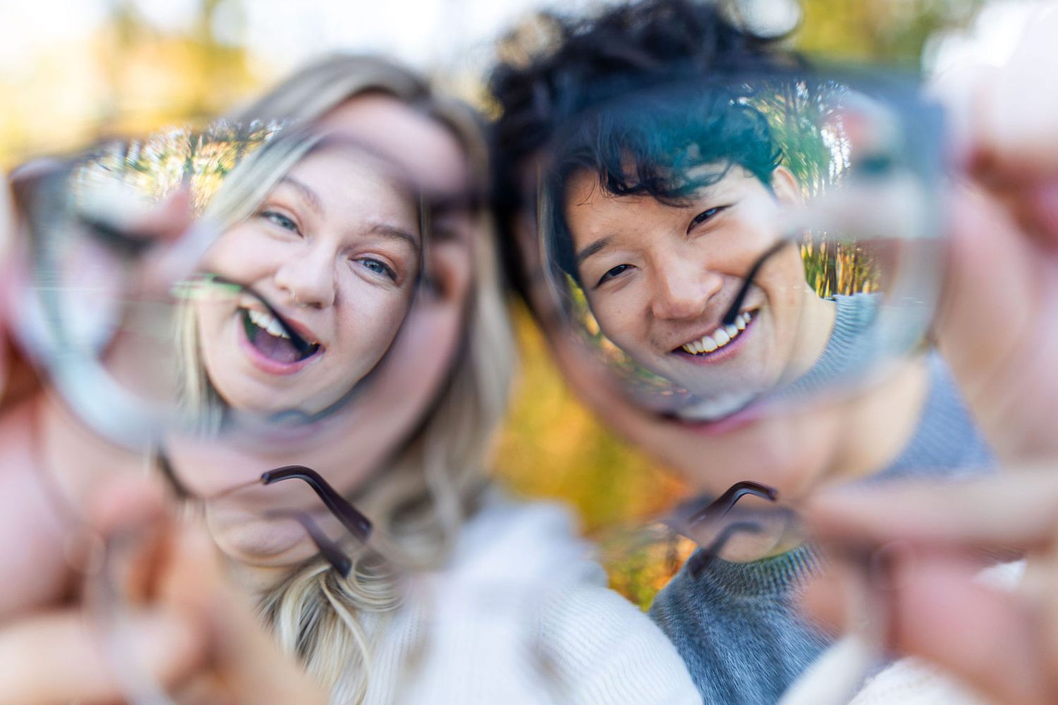 Two happy women laughing and holding eyeglasses up to the camera outdoors in autumn.