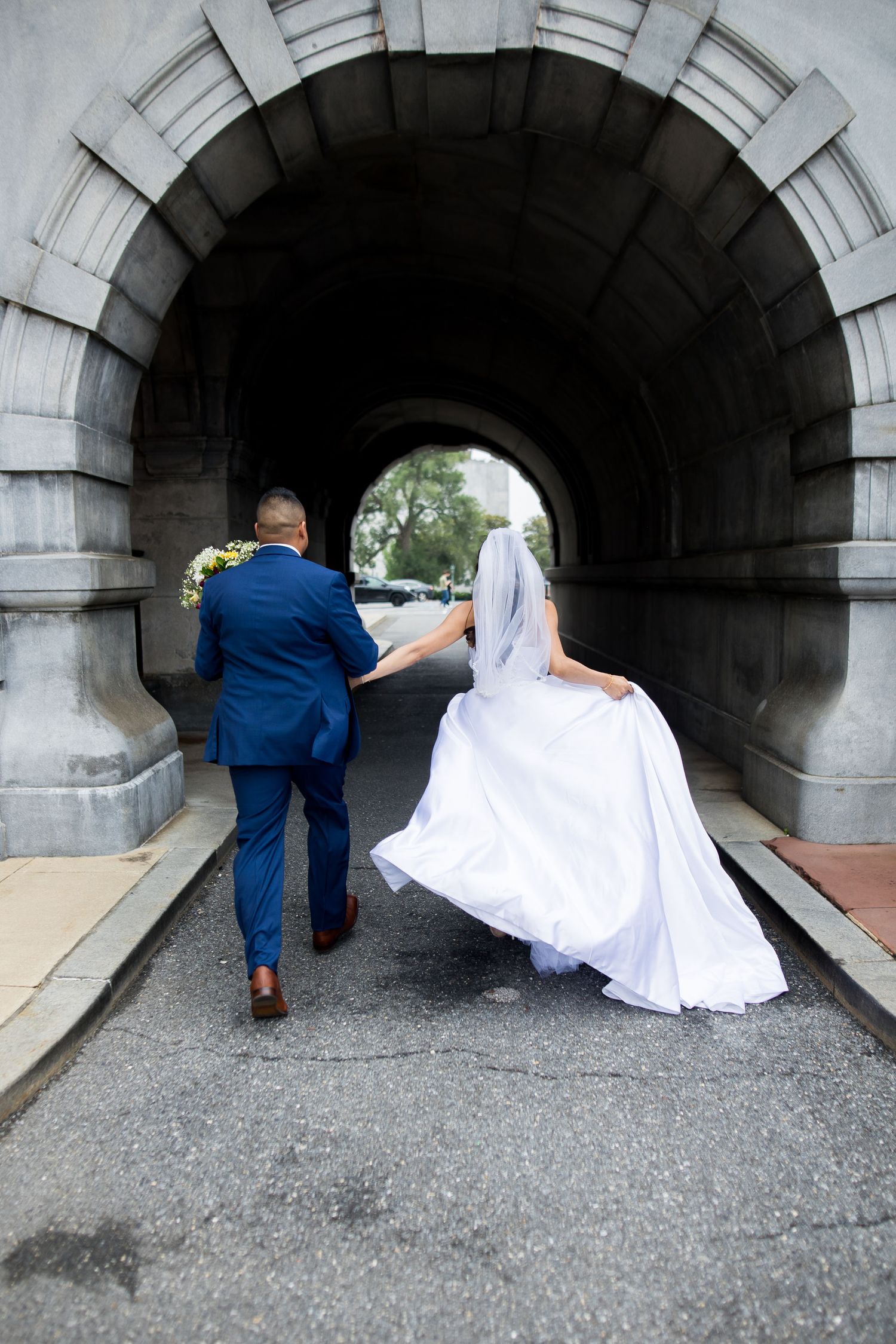 Bride and groom walking hand-in-hand through the stone archway tunnel at the Library of Congress in Washington, DC.