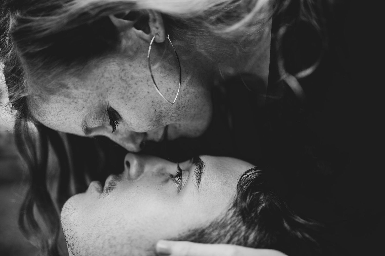 Black and white photo of a romantic couple sharing an intimate moment, almost kissing, close-up portrait.
