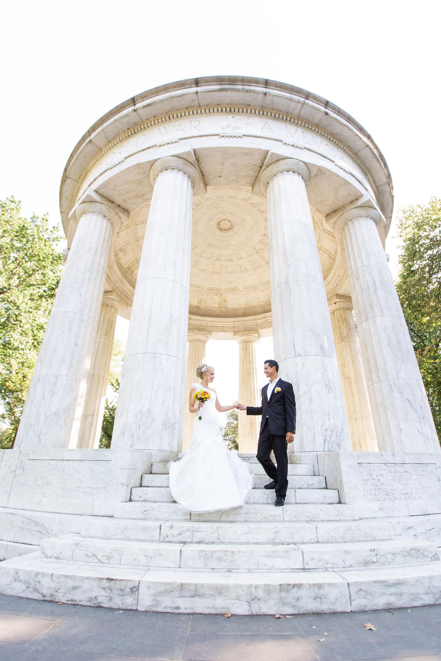 Bride and groom hold hands on marble steps of the classical rotunda and white columns at the World War I Memorial in Washington, DC.