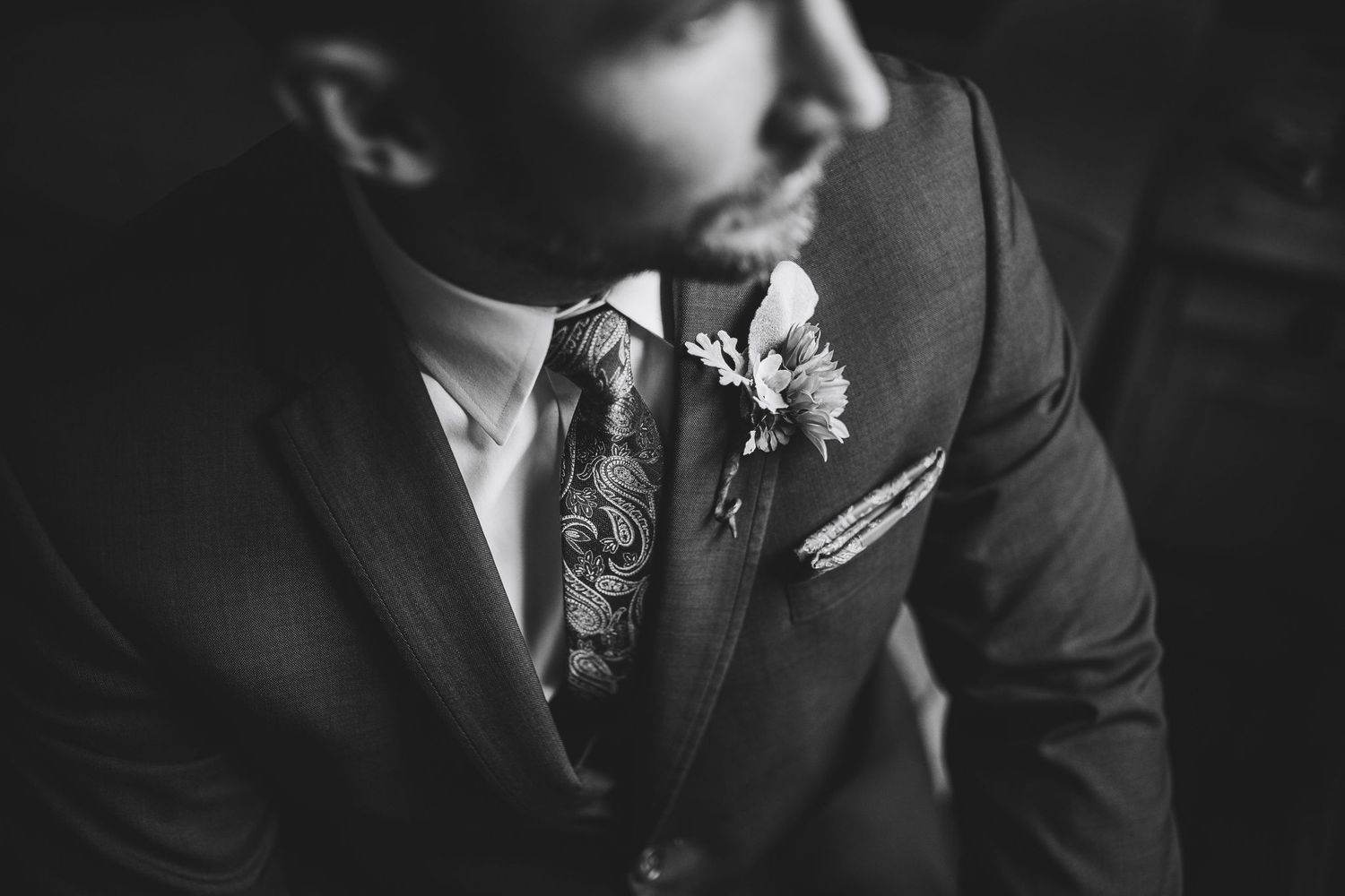 Black and white photo of a groom in a suit with floral tie and boutonniere on his wedding day.