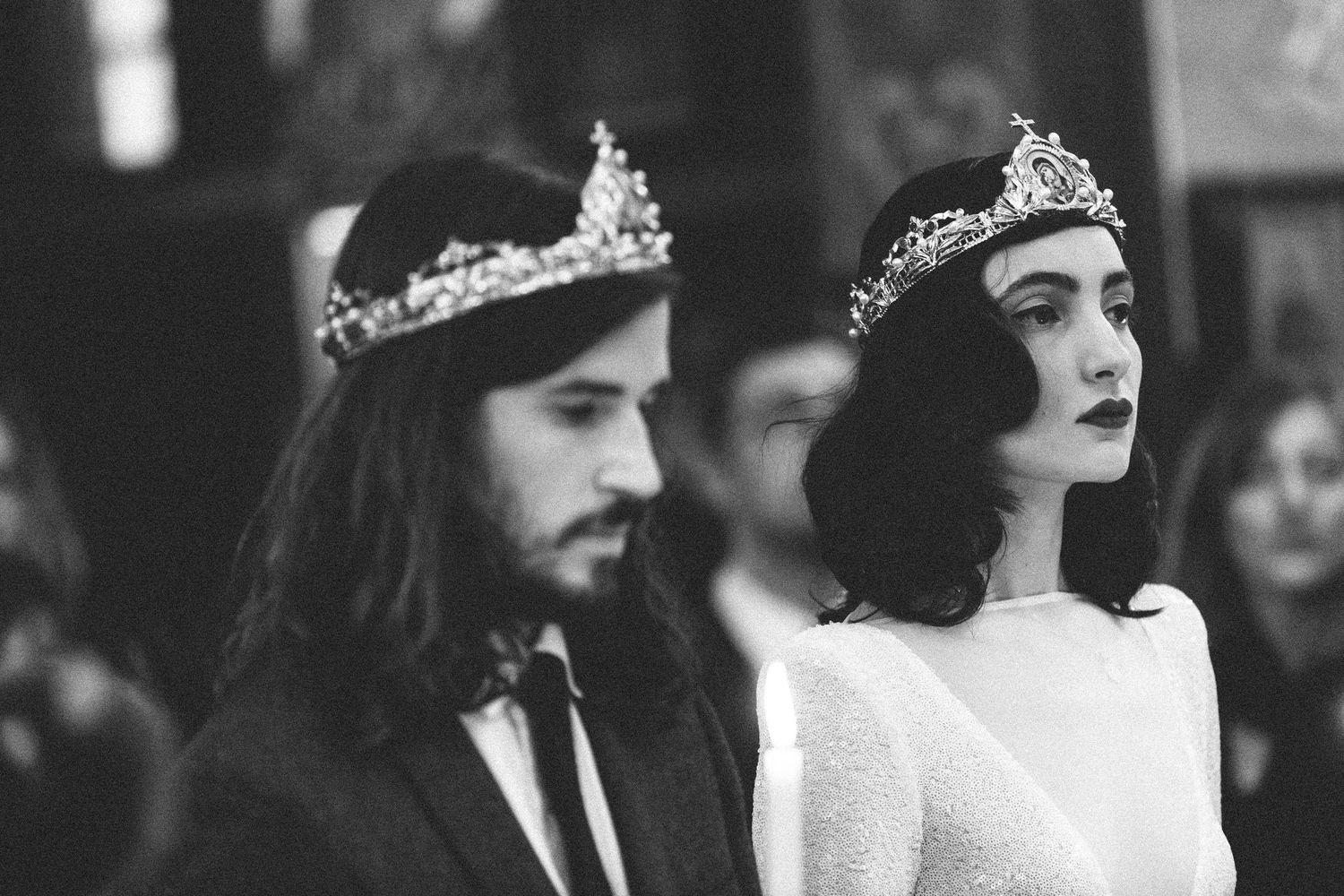 Black and white photo of a bride and groom wearing ornate crowns during a wedding ceremony.