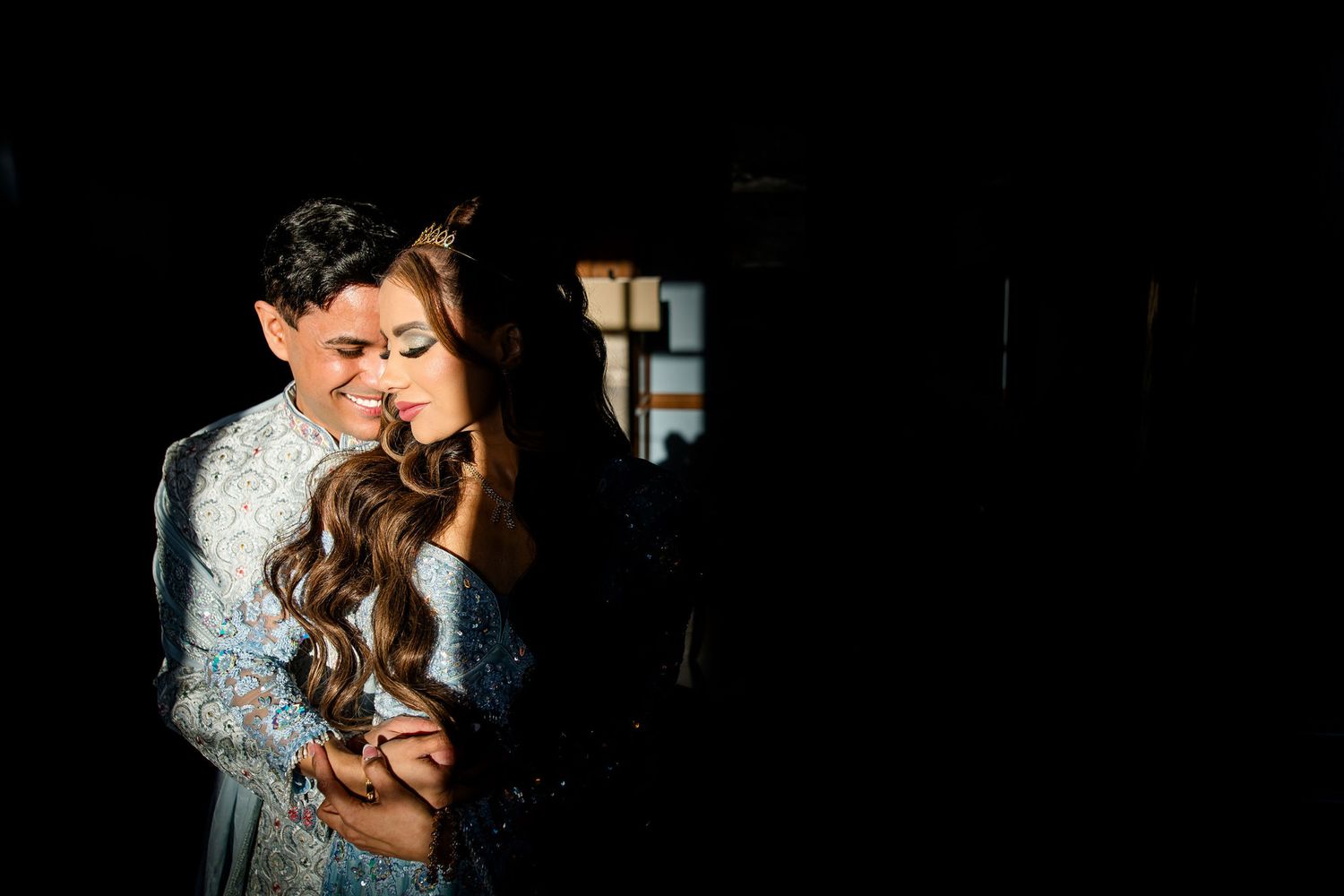 Couple embracing tenderly in dramatic dark lighting, wearing elegant formal attire at a wedding celebration.