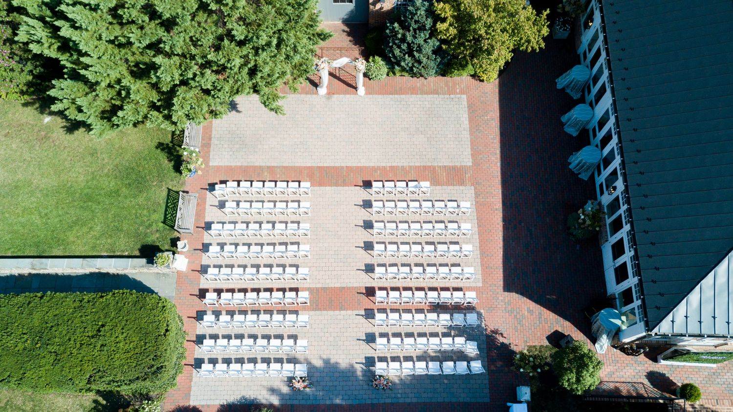 Aerial view of outdoor wedding ceremony setup with rows of white chairs arranged on a brick patio.