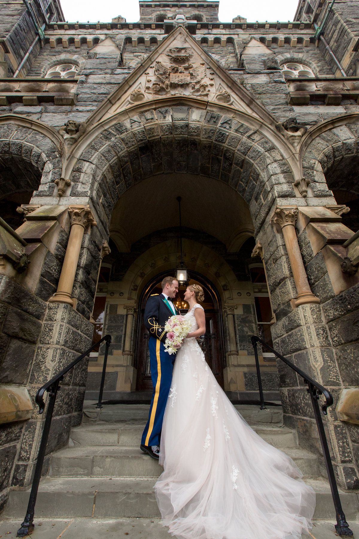 Bride and groom share a romantic kiss on stone steps of a Gothic cathedral in wedding attire.
