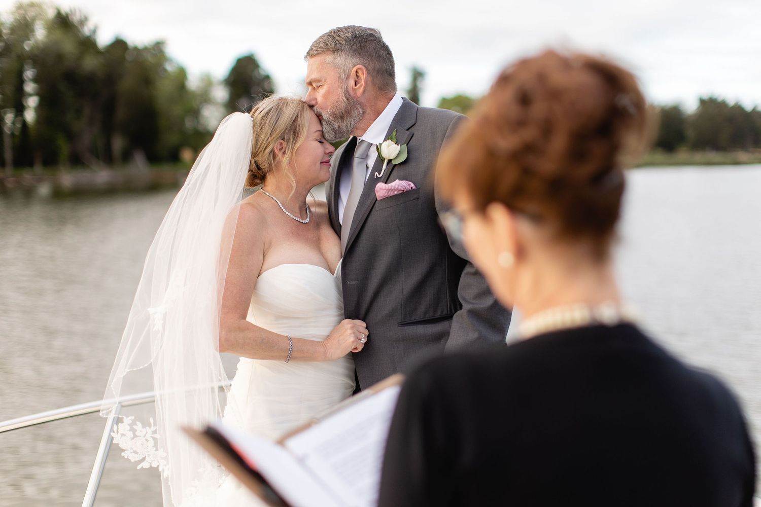 Bride and groom share an intimate moment during outdoor waterfront wedding ceremony officiated by a red-haired officiant.