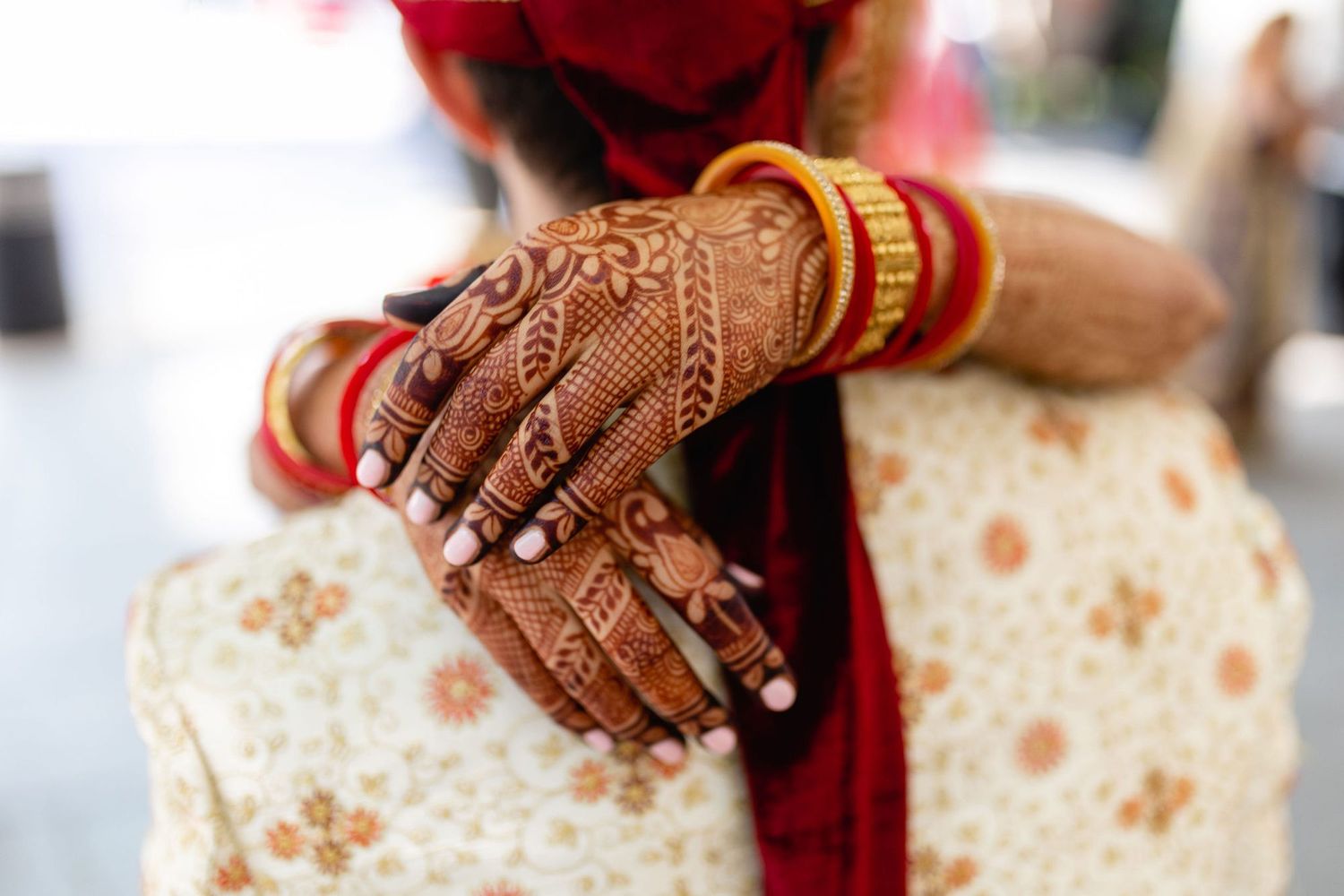 Close-up of bride's hands adorned with intricate henna mehndi designs and gold bangles during Indian wedding ceremony.