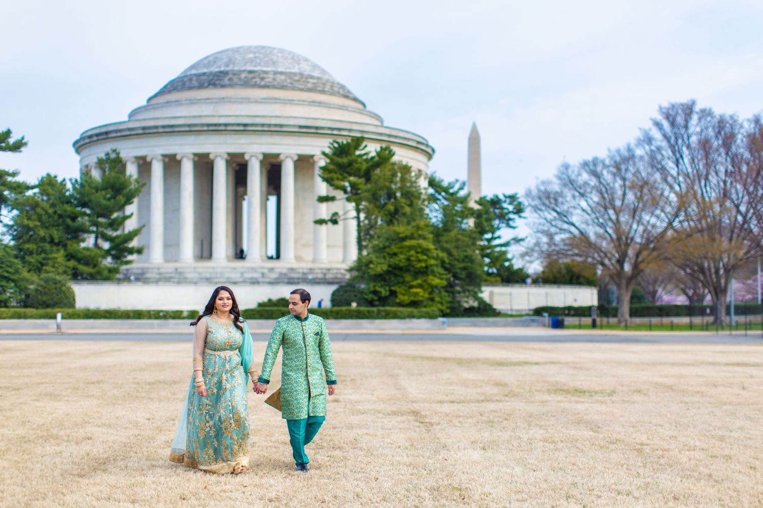 Indian couple in teal traditional attire holding hands near Jefferson Memorial and Washington Monument, DC.