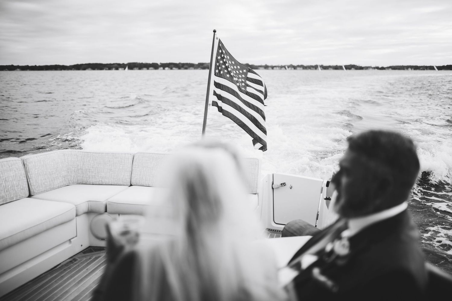 Bride and groom on a luxury boat with American flag waving over open water on their wedding day.