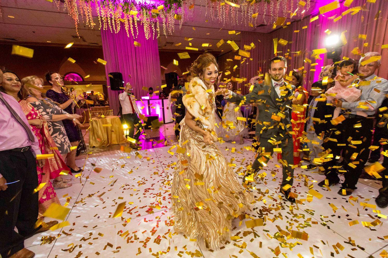 Woman in gold dress dancing joyfully as golden confetti rains down at an elegant celebration event.