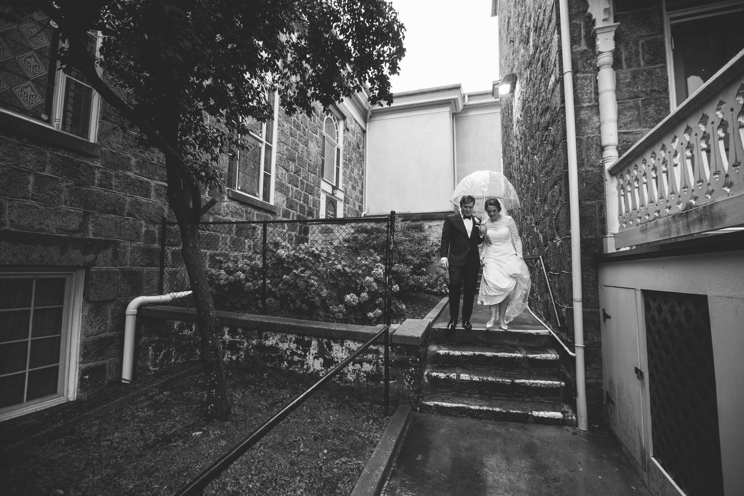 Black and white photo of a bride and groom walking up stone steps outside a historic building on their wedding day.