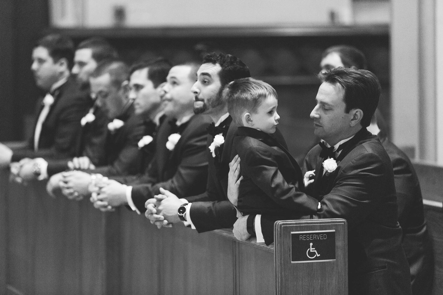Groomsmen and ring bearer standing at altar during wedding ceremony in black and white.