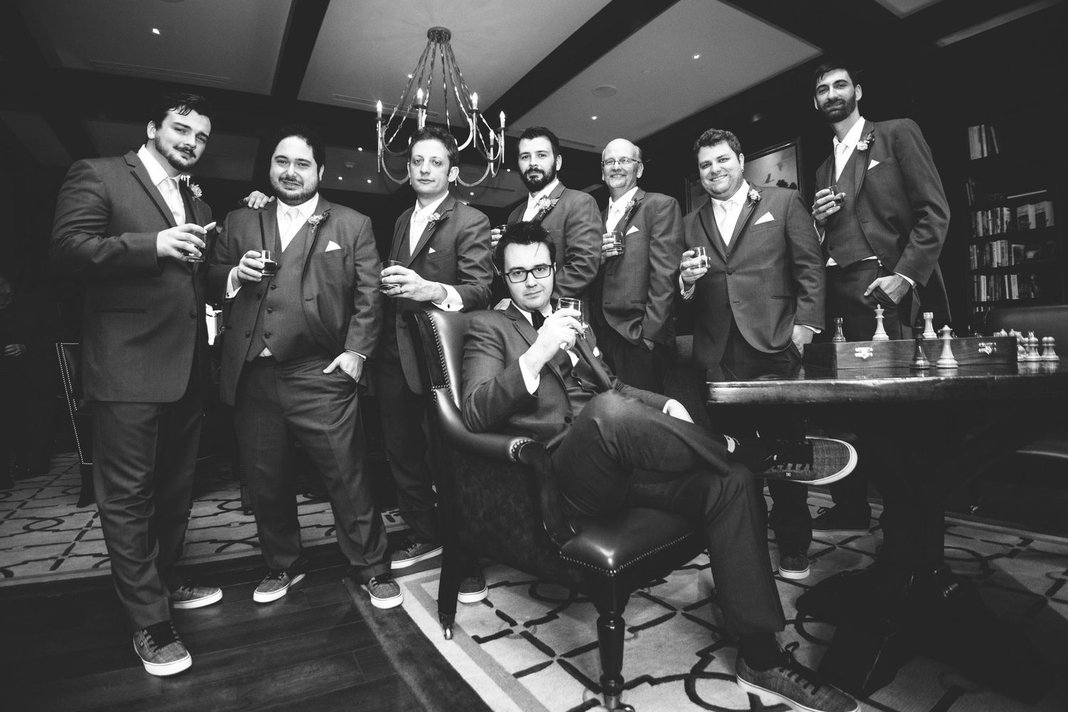 Group of groomsmen in suits posing with drinks in elegant black and white wedding photo.