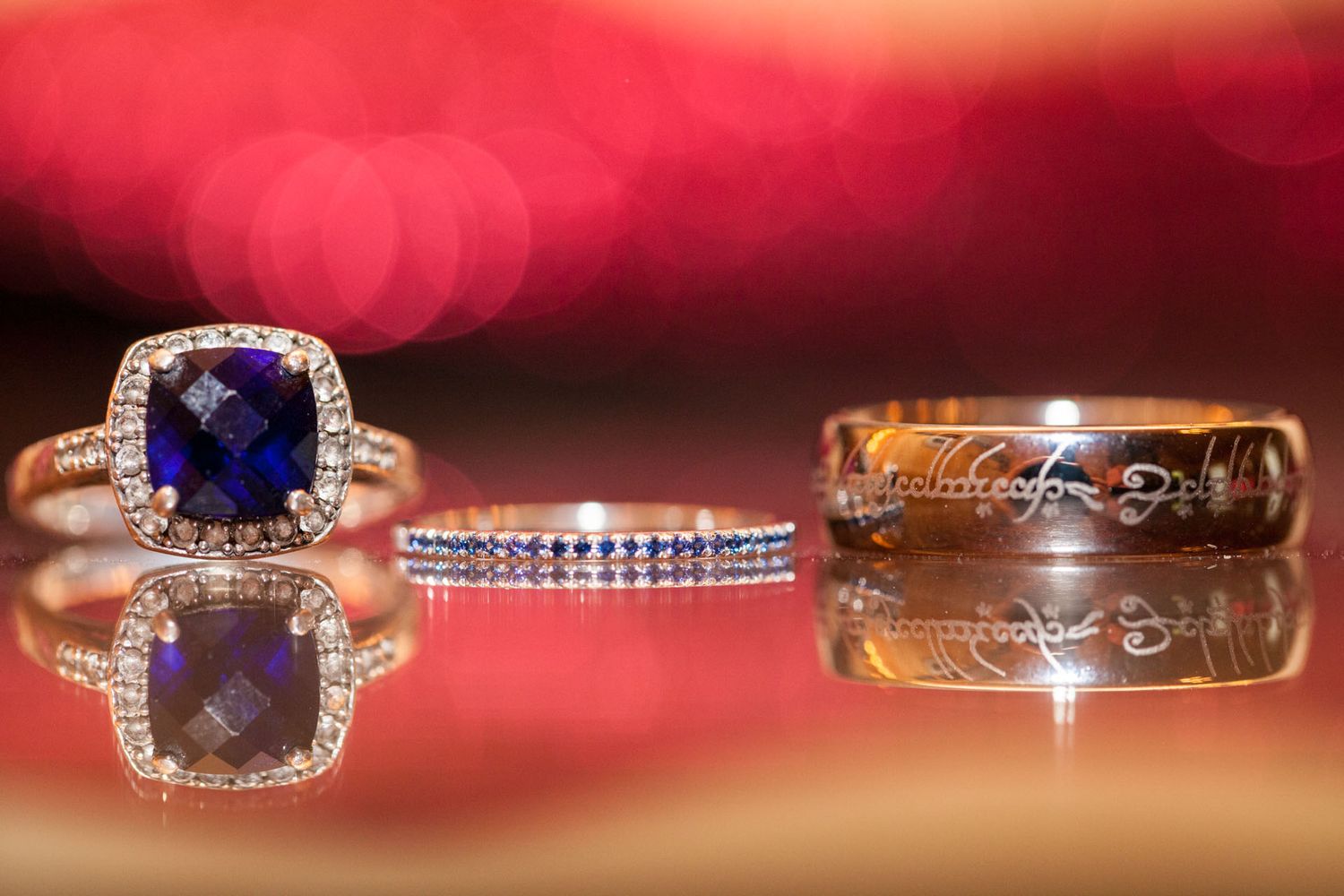 Three elegant rings displayed together, featuring a sapphire halo engagement ring, diamond band, and engraved gold ring.
