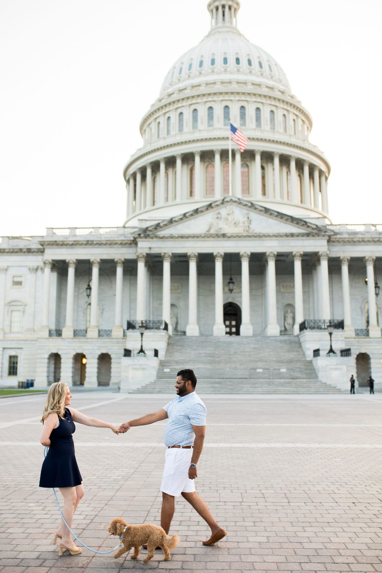 Couple holding hands walking a golden dog in front of the U.S. Capitol building in Washington, D.C.