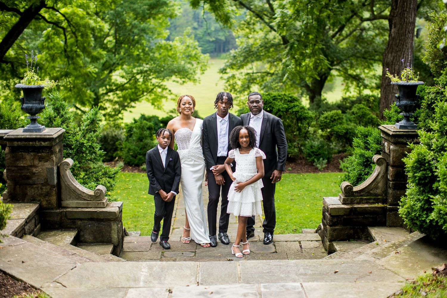 A joyful family poses on stone steps in a lush garden, dressed in elegant wedding attire.