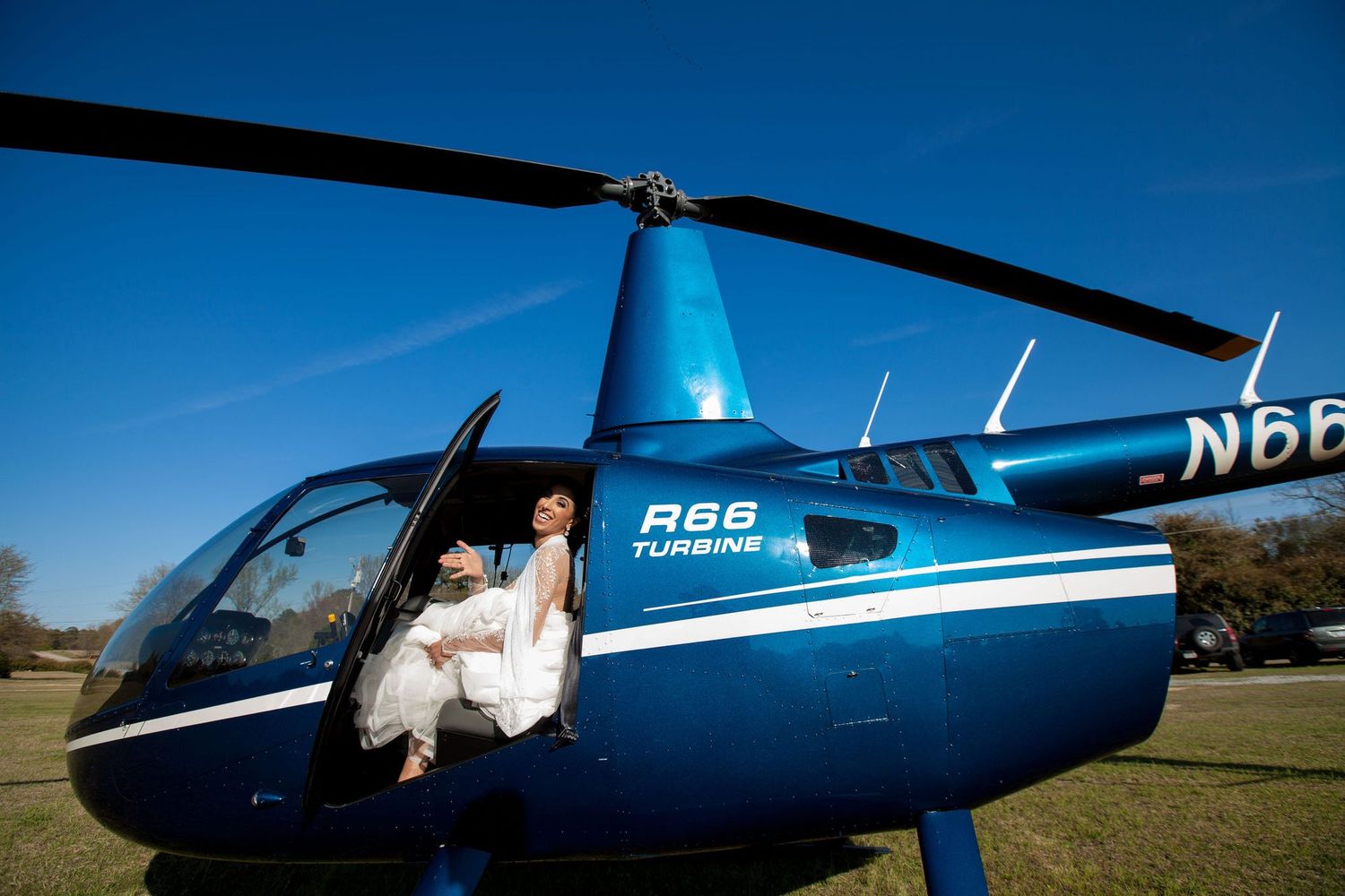 Bride in white dress sitting in a blue Robinson R66 Turbine helicopter on a sunny day.