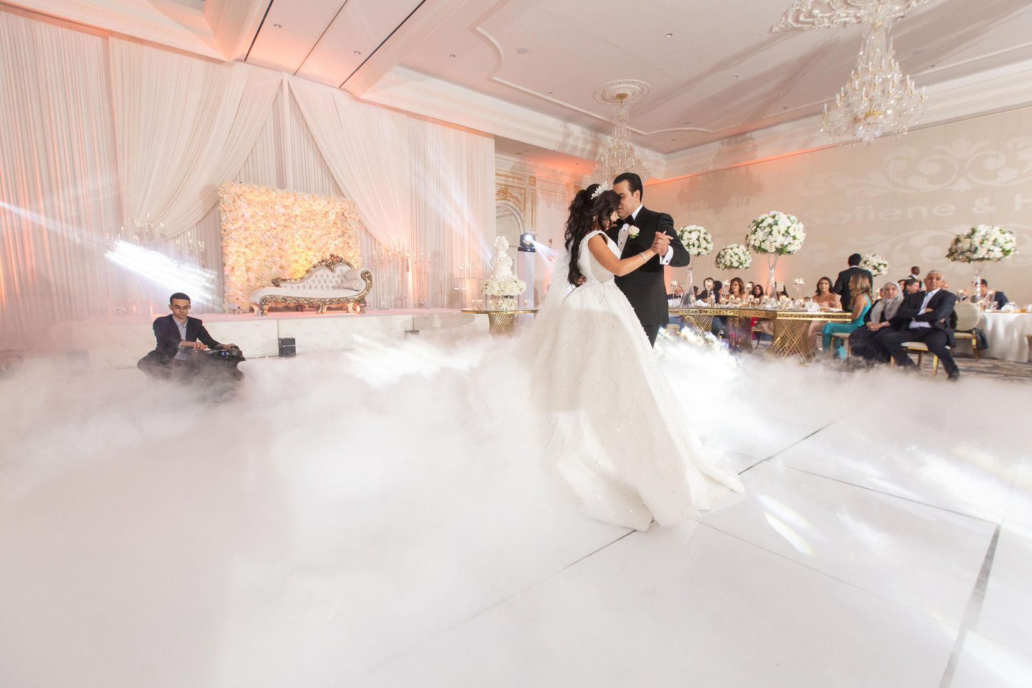 Bride and groom share first dance on a cloud-filled dance floor at an elegant white wedding reception.