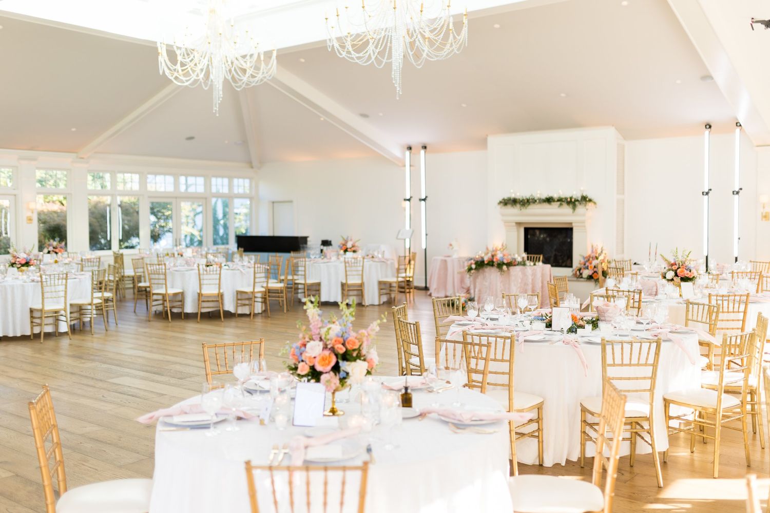 Bright wedding reception hall with gold chiavari chairs, white tablecloths, floral centerpieces, and vaulted ceilings.