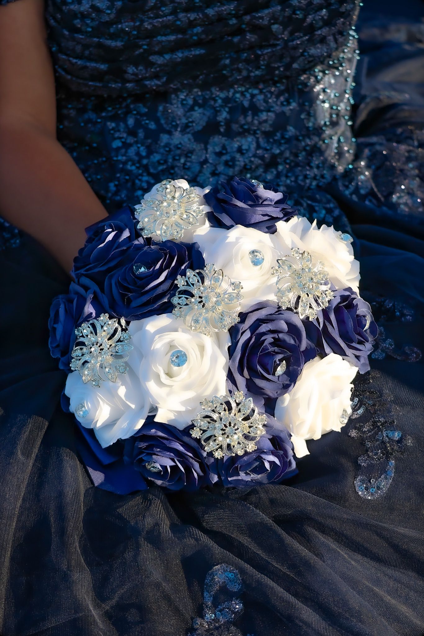 Faux flower bouquet made from satin ribbon that is blue and white to match the quinceañera theme and dress with rhinestone embellishments.