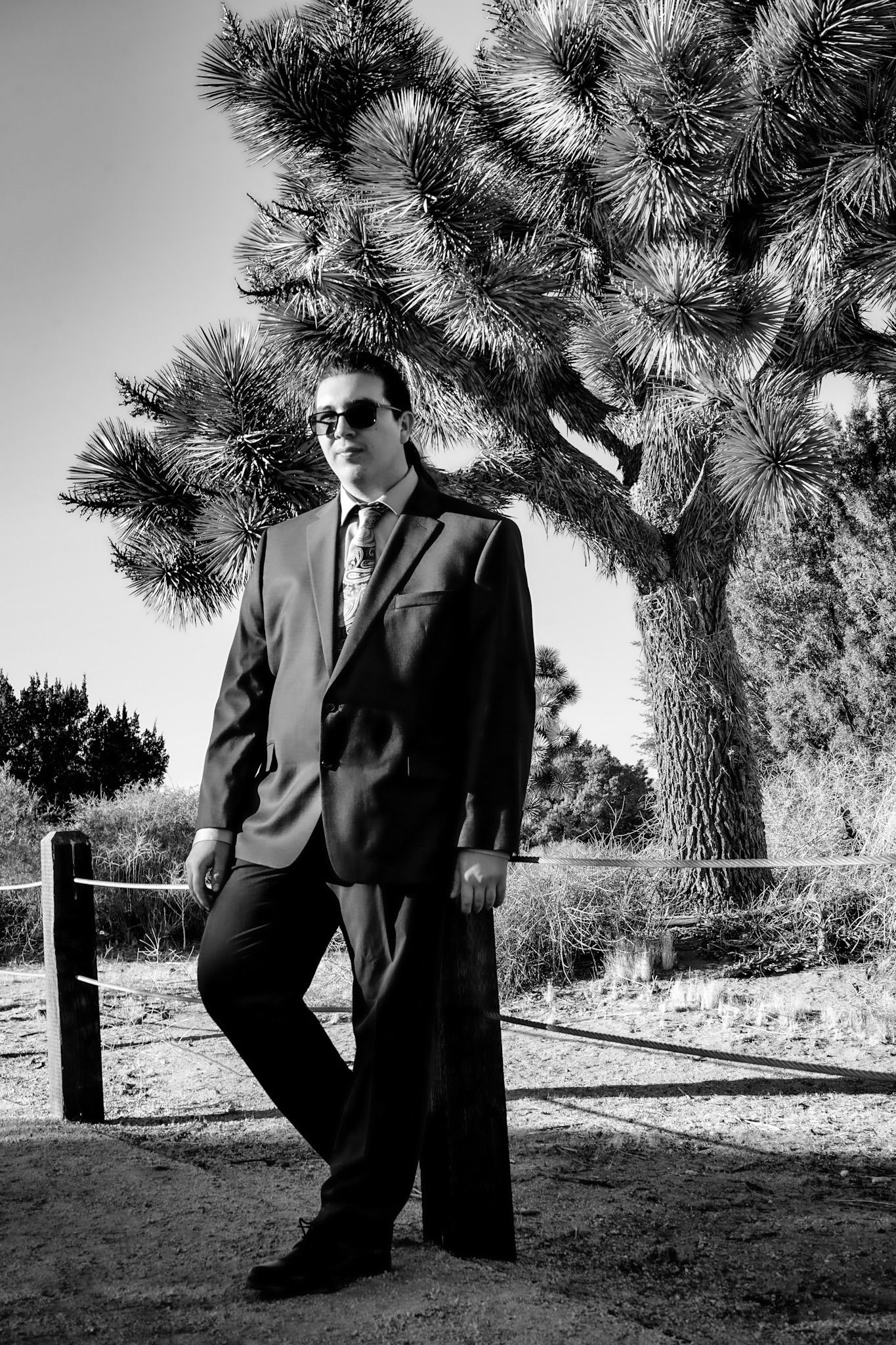 Black and white portrait of high school graduate leaning against a post, looking off into the distance.