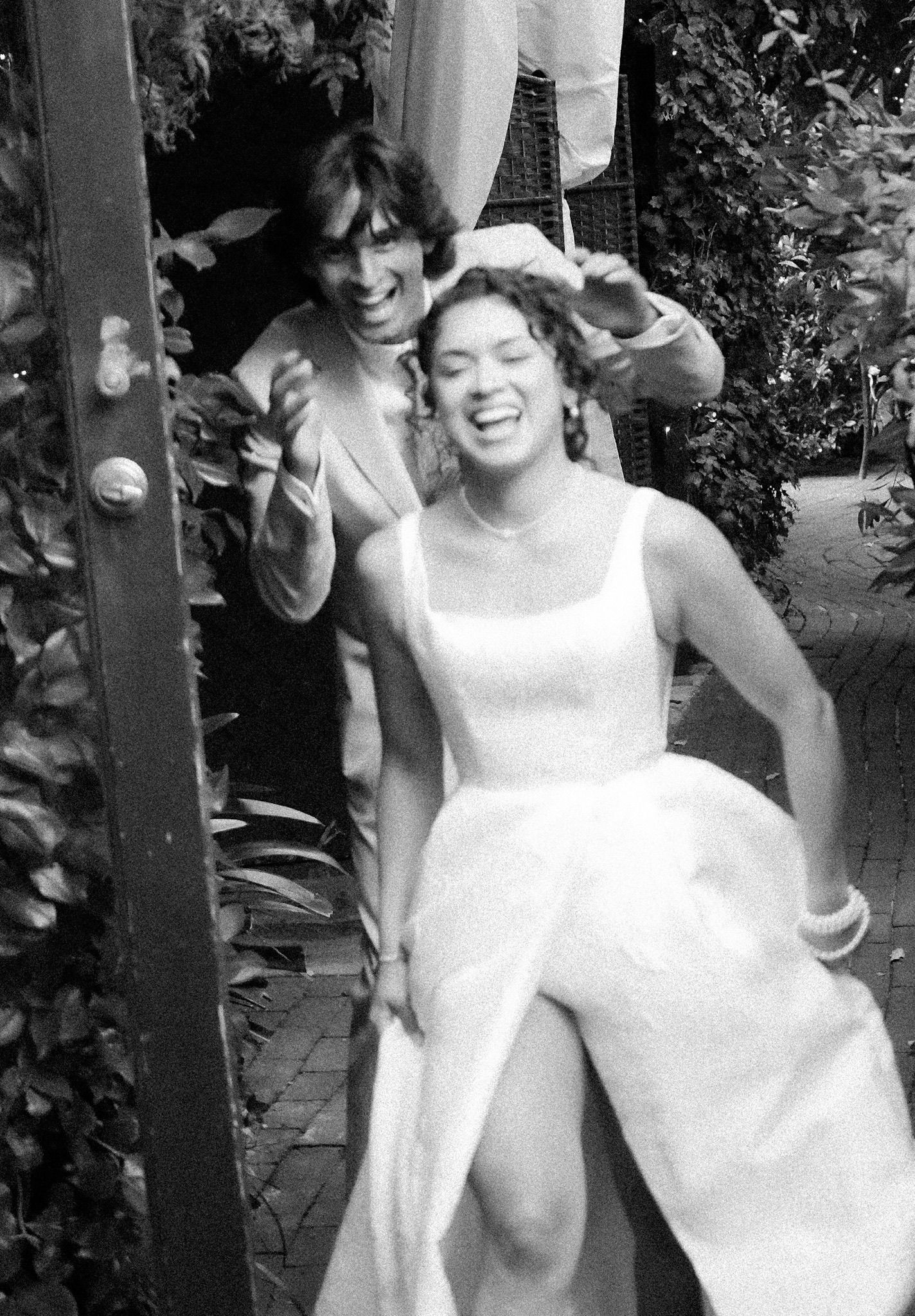 Bride running and groom chasing her playfully outdoors during a post-ceremony wedding session, both smiling and laughing.
