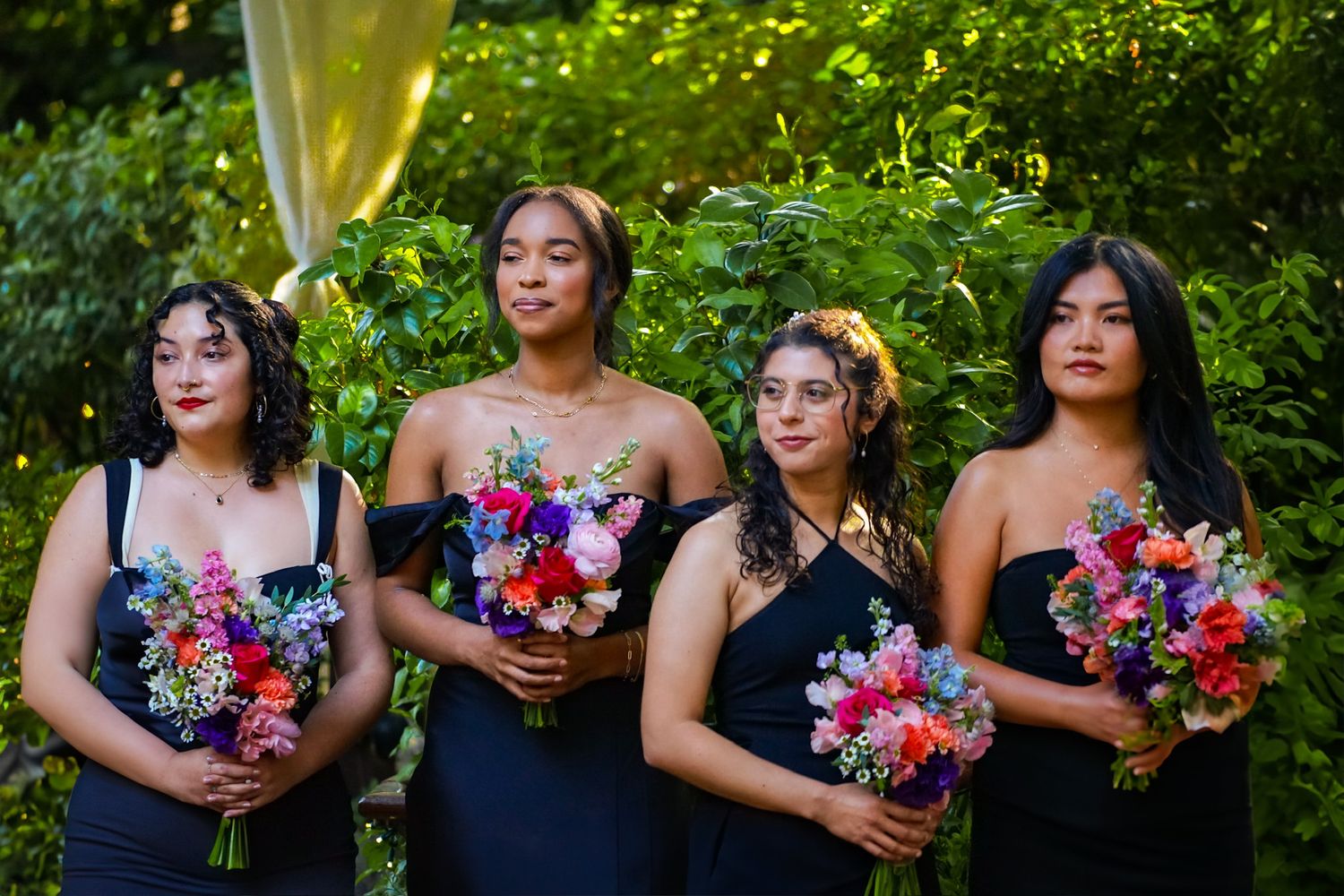 Four bridesmaid stand near the altar all wearing deep navy dresses holding matching colorful bouquets, onlooking as the bride walks in.