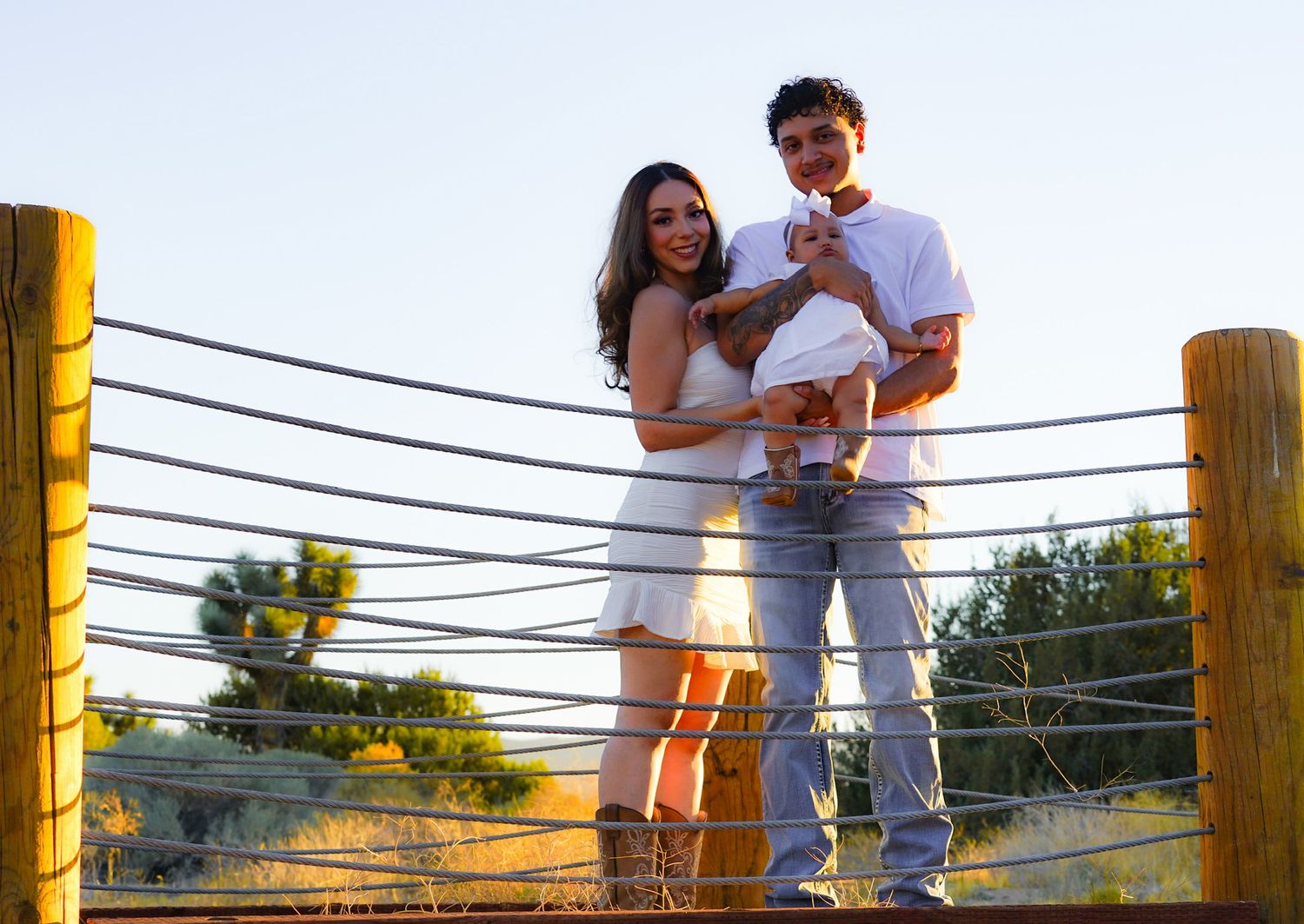 Family of three dressed in matching white attire, warmly embracing one another and holding their infant daughter for a portrait.